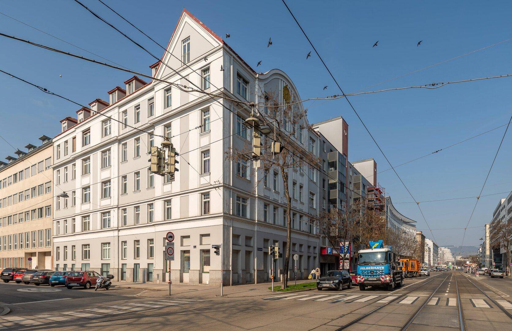 Historisches Eckgebäude an einer belebten Straße mit Straßenbahnen.
