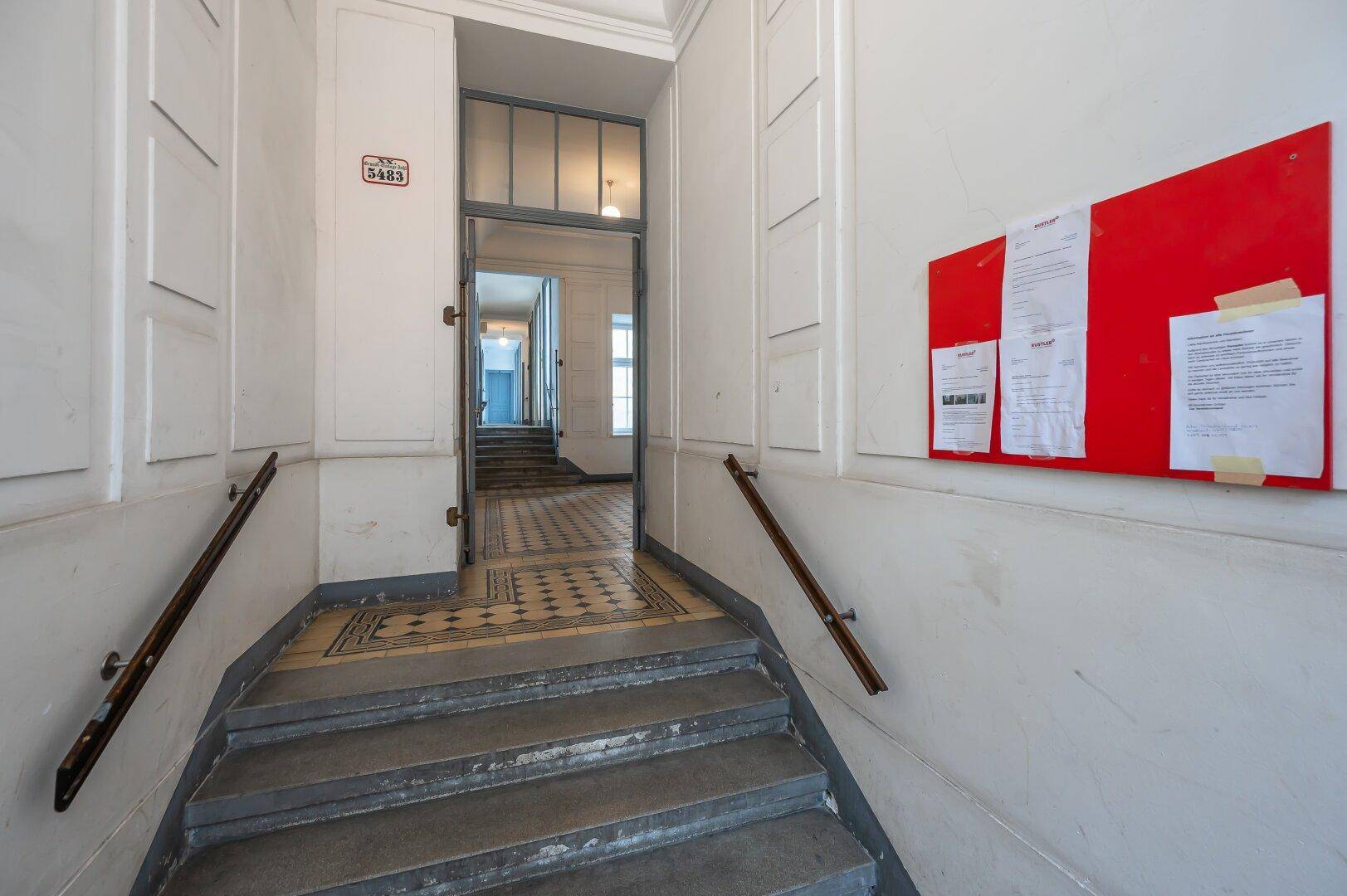 Treppenaufgang im Altbau mit hohen Wänden und traditionellen Fliesen.