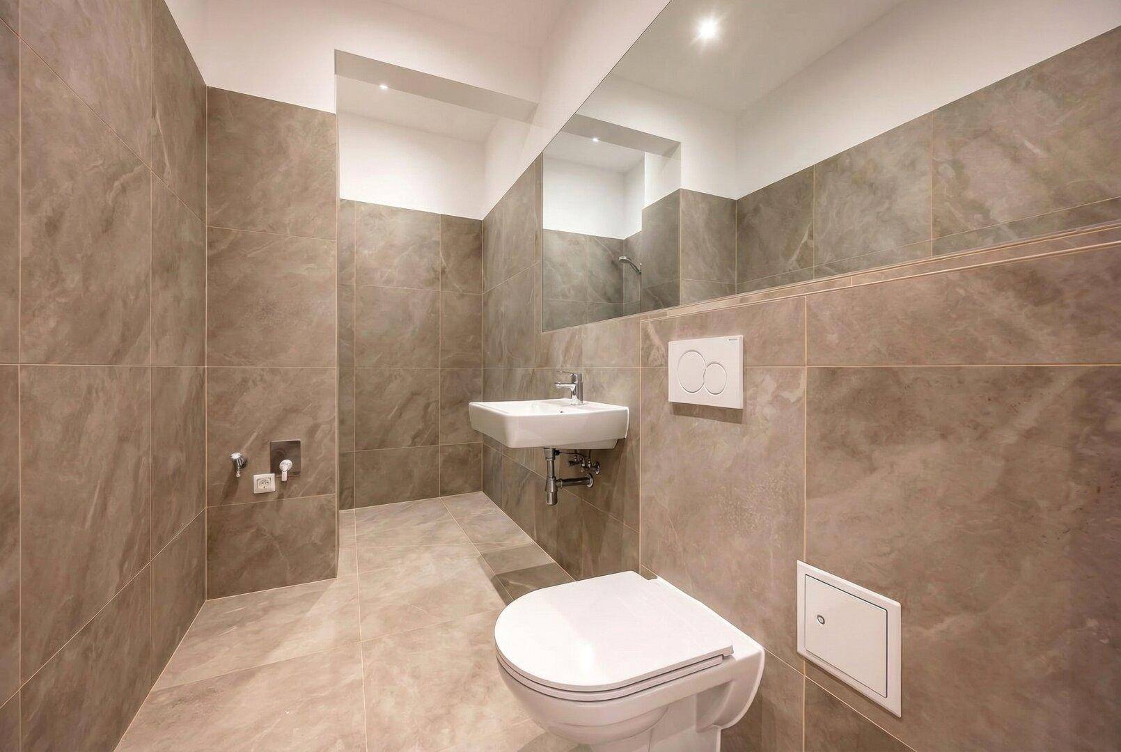 Modernes Badezimmer mit großformatigen Fliesen, wandhängendem WC und Waschbecken.