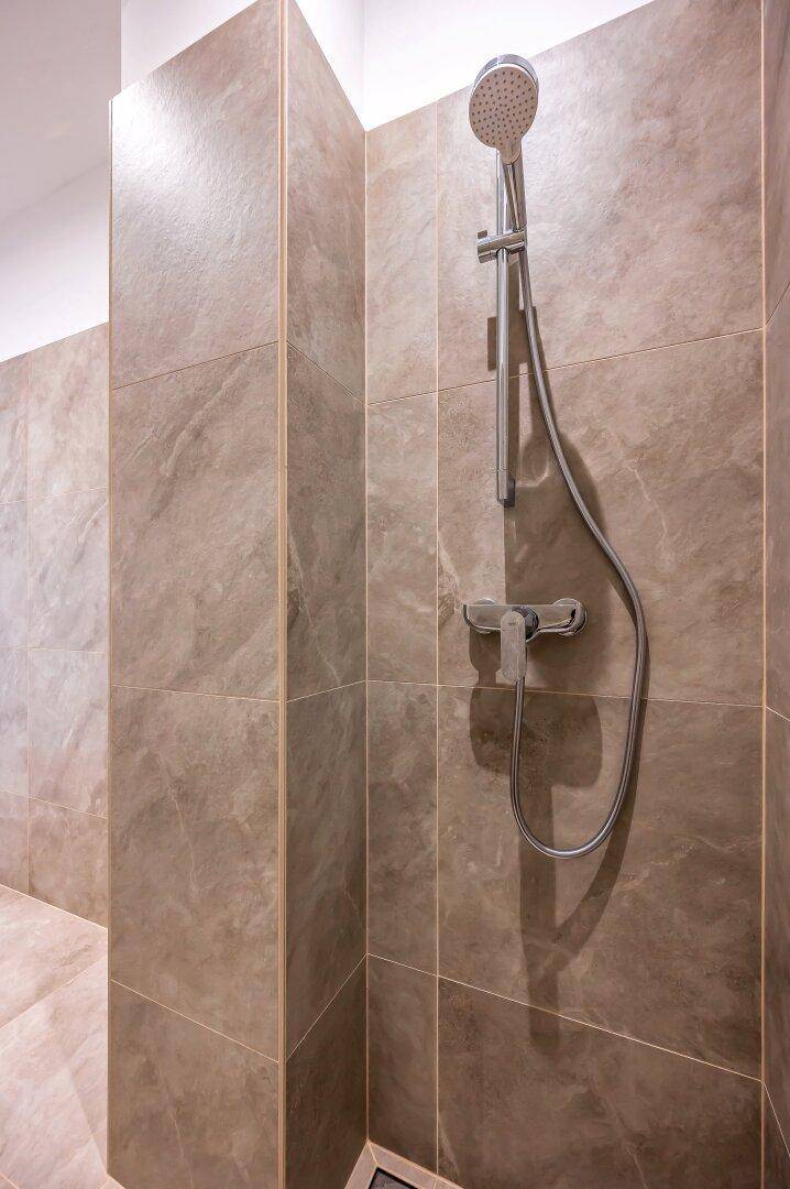 Moderne Duschkabine mit großformatigen Fliesen und Handbrause in einem zeitgemäßen Badezimmer.