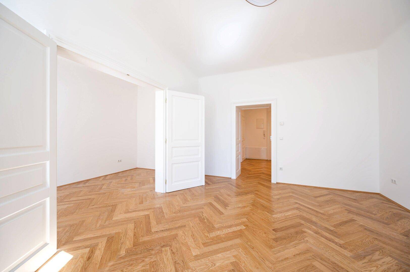 Heller Raum mit Fischgrätparkett und hohen Türen, der Offenheit und Eleganz ausstrahlt.