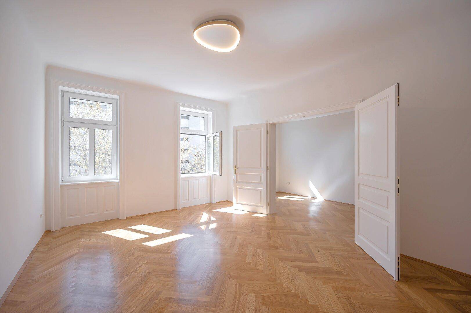 Geräumiges, helles Zimmer mit Fischgrätparkett und hohen Fenstern, bereit zur individuellen Gestaltung.
