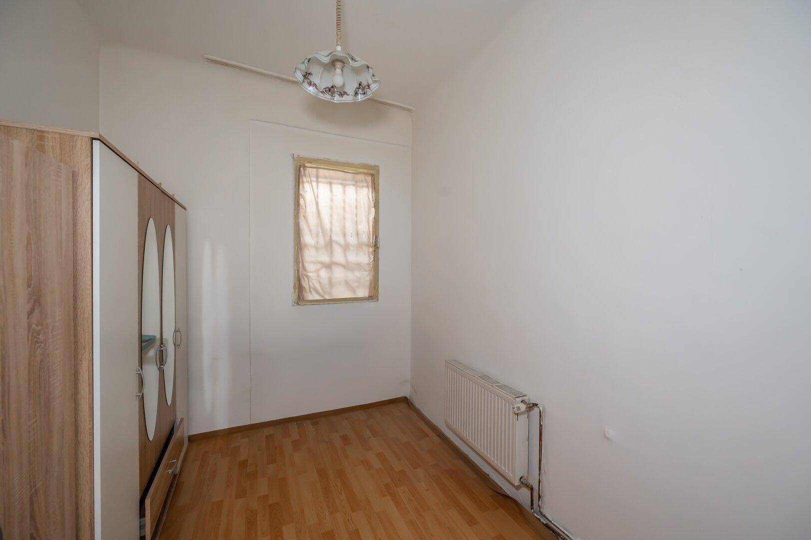 Kleines, helles Zimmer mit Holzfußboden und Heizkörper, vielseitig nutzbar.