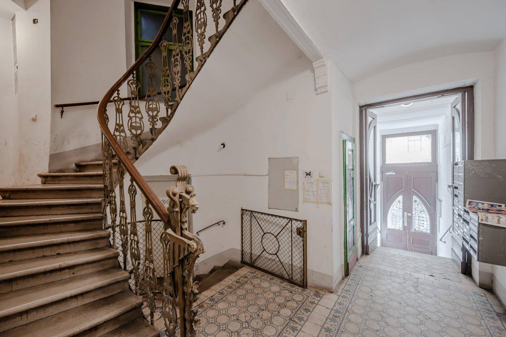 Elegantes Treppenhaus eines Altbaus mit schmiedeeisernem Geländer und Eingangsbereich.