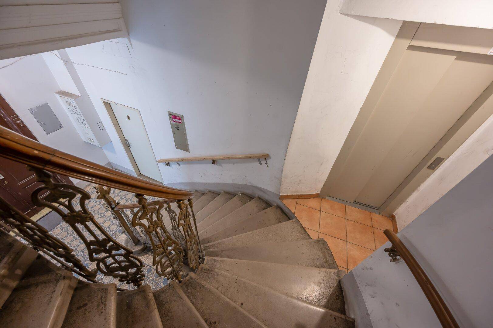 Wendeltreppe mit historischem Geländer und Blick auf den Aufzug im Treppenhaus.