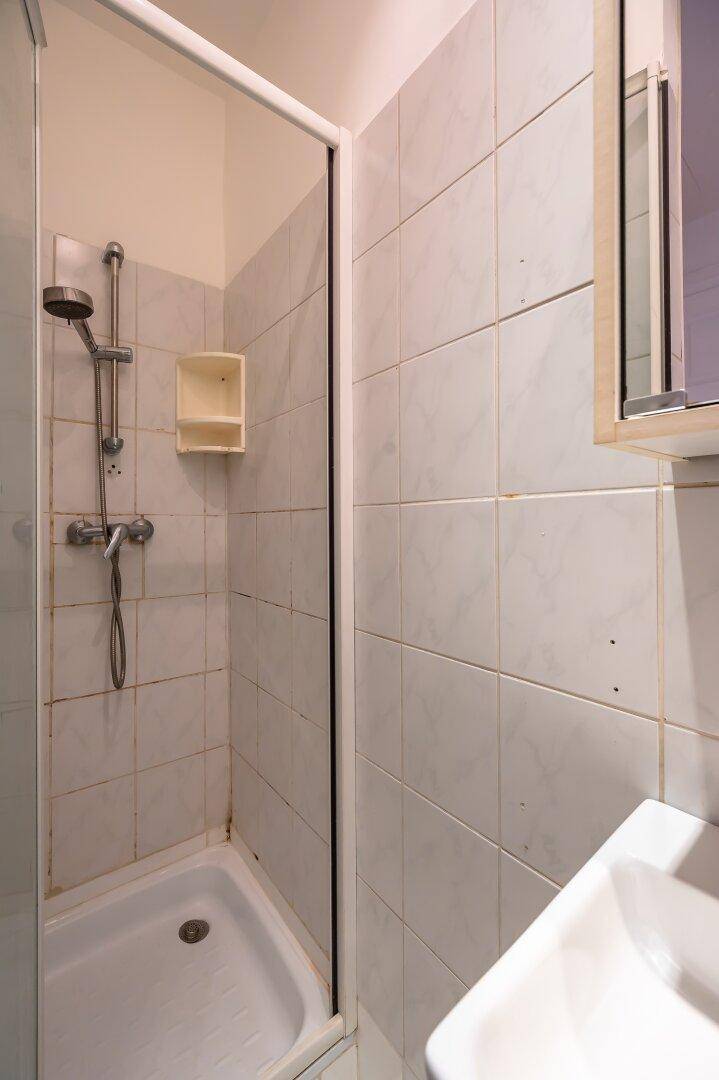 Kleines Badezimmer mit Duschkabine, weißen Fliesen und einem Waschbecken mit Spiegelschrank.