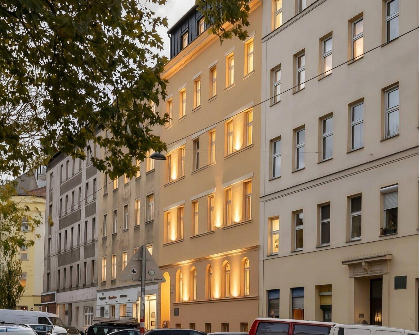 Renovierte Fassade eines Mehrfamilienhauses mit beleuchteten Fenstern in städtischer Umgebung.