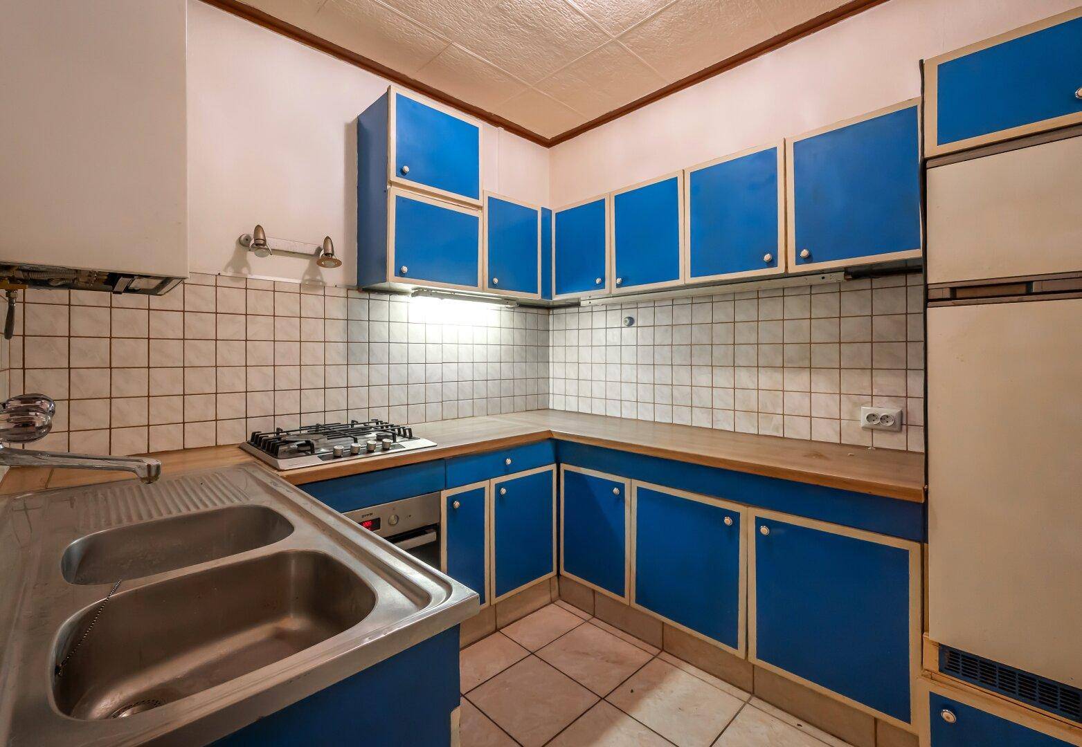 Funktionale Küche mit blauen Schränken, Gasherd, Backofen und Doppelspüle.