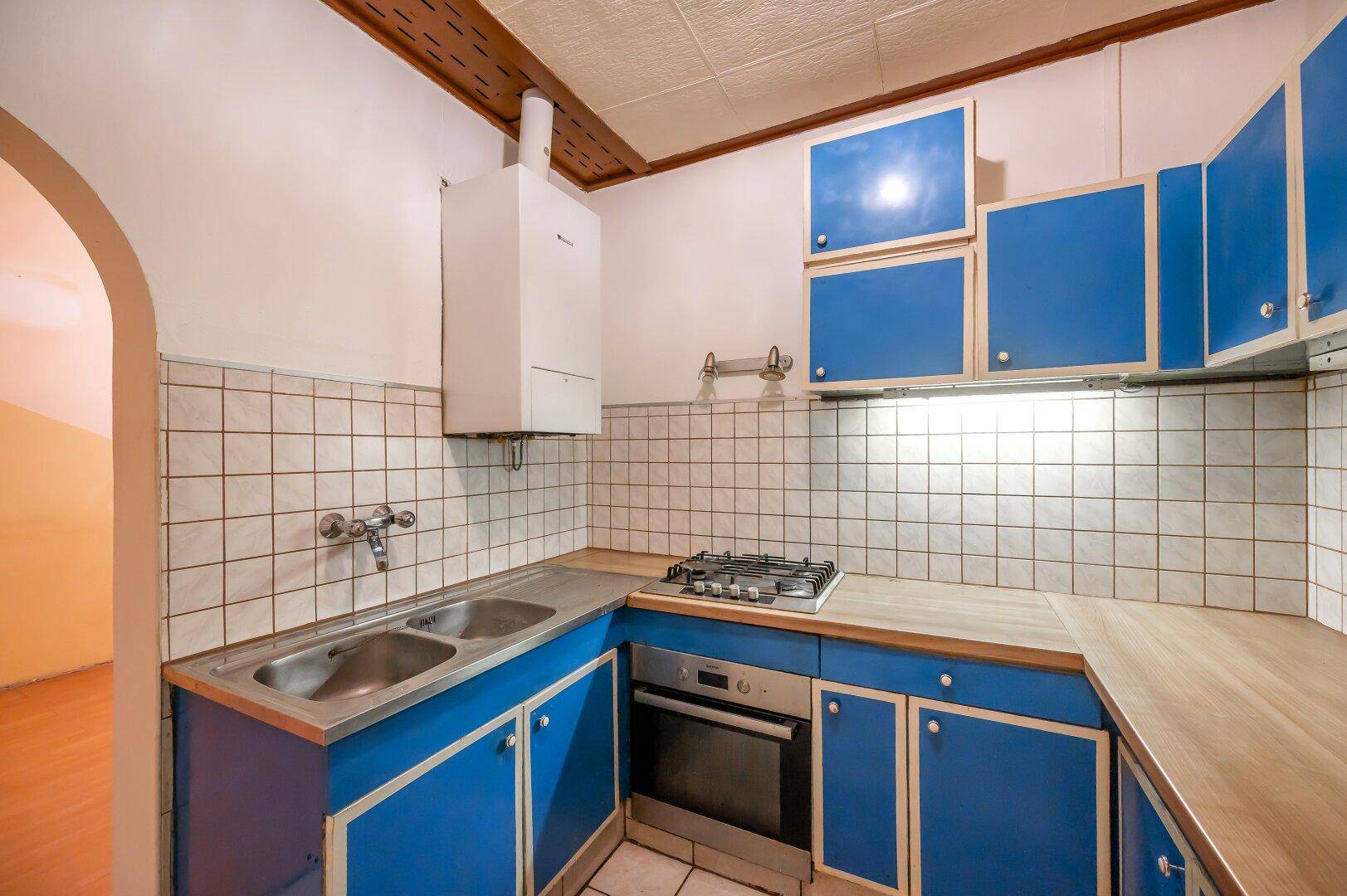 Blaue Küche mit Gasherd, Backofen, Doppelspüle und einem an der Wand montierten Boiler.