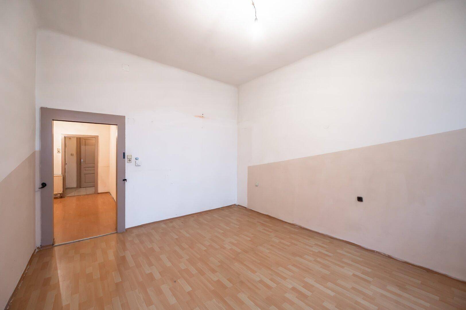 Geräumiges Zimmer mit Holzfußboden und Zugang zu einem Flur, ideal für verschiedene Nutzungen.