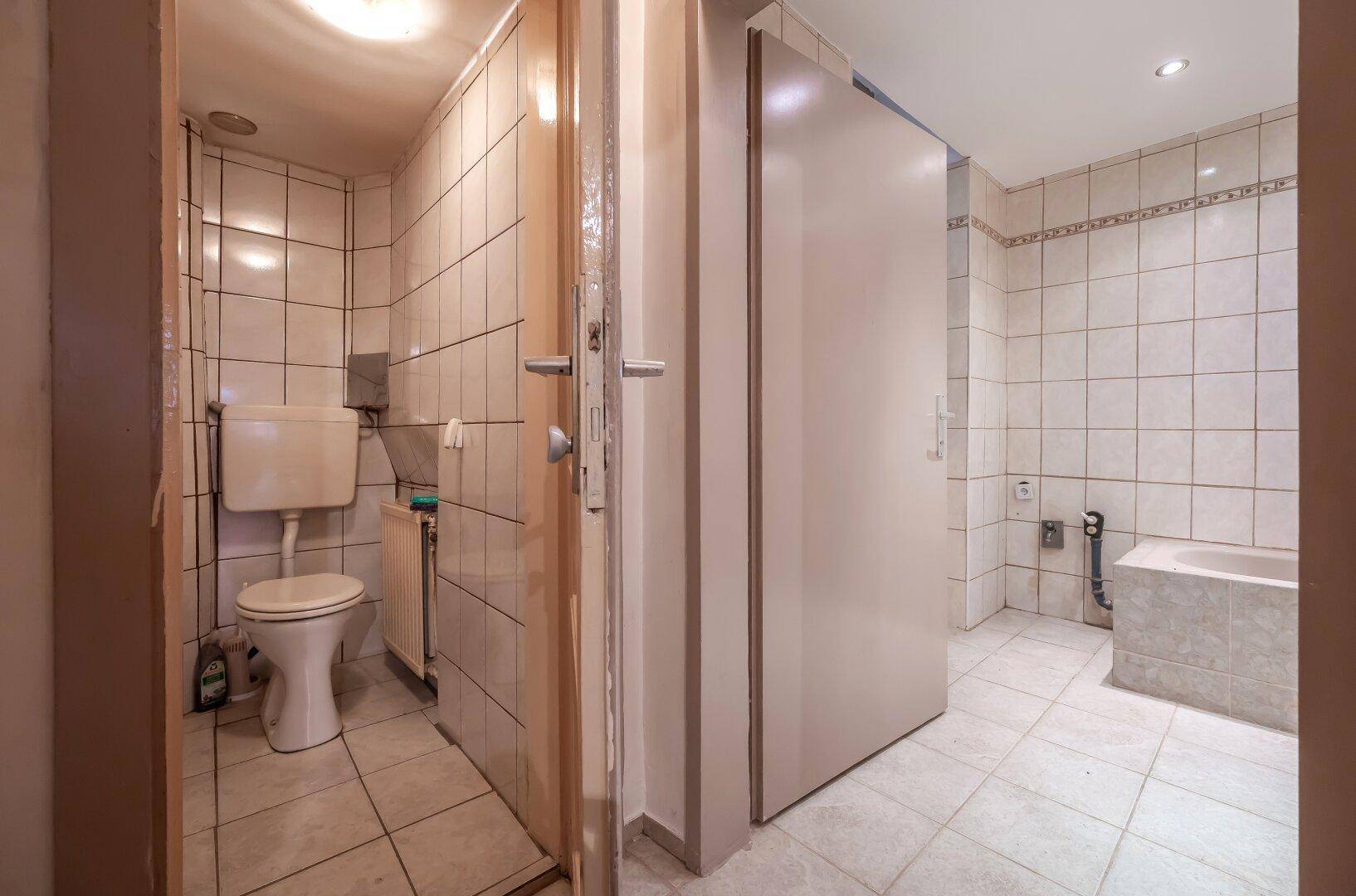 Badezimmer mit beigen Fliesen und separatem WC-Bereich, ausgestattet mit Toilette.