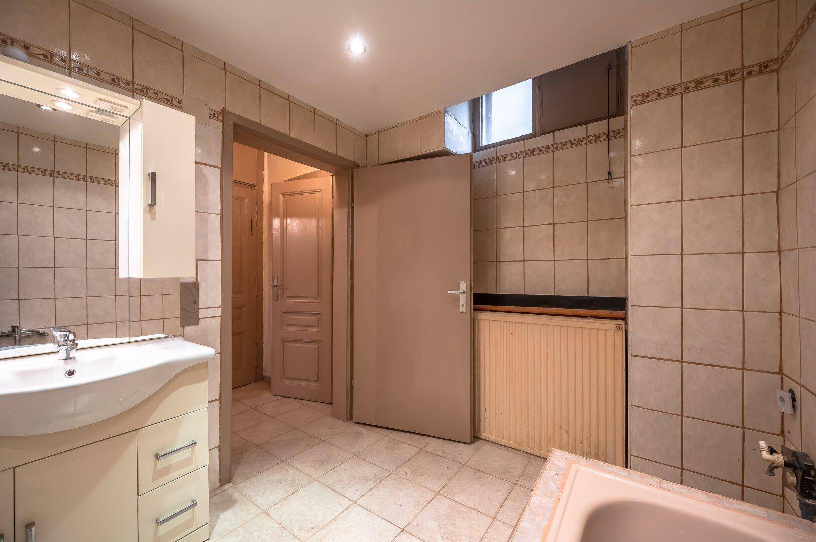 Helles Badezimmer mit beigen Fliesen, Waschtisch und kleinem Fenster für natürliche Belüftung.