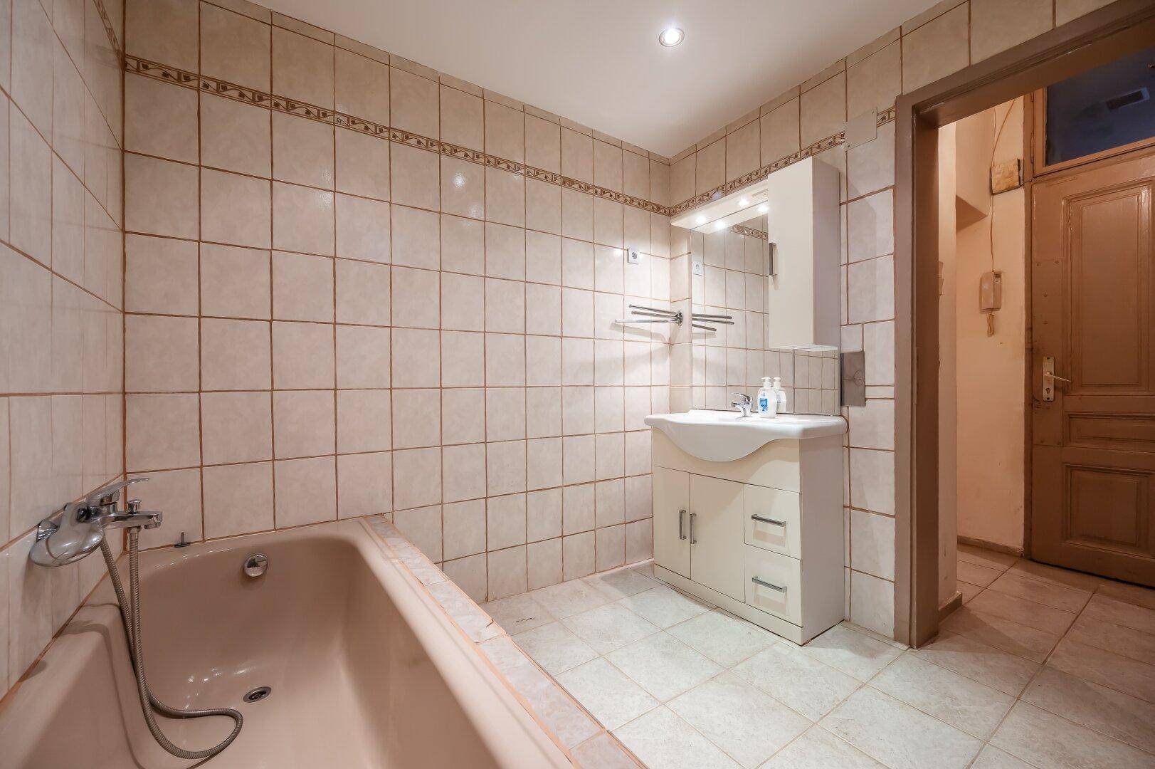 Gefliestes Badezimmer mit Badewanne, Einzelwaschbecken und Spiegelschrank.