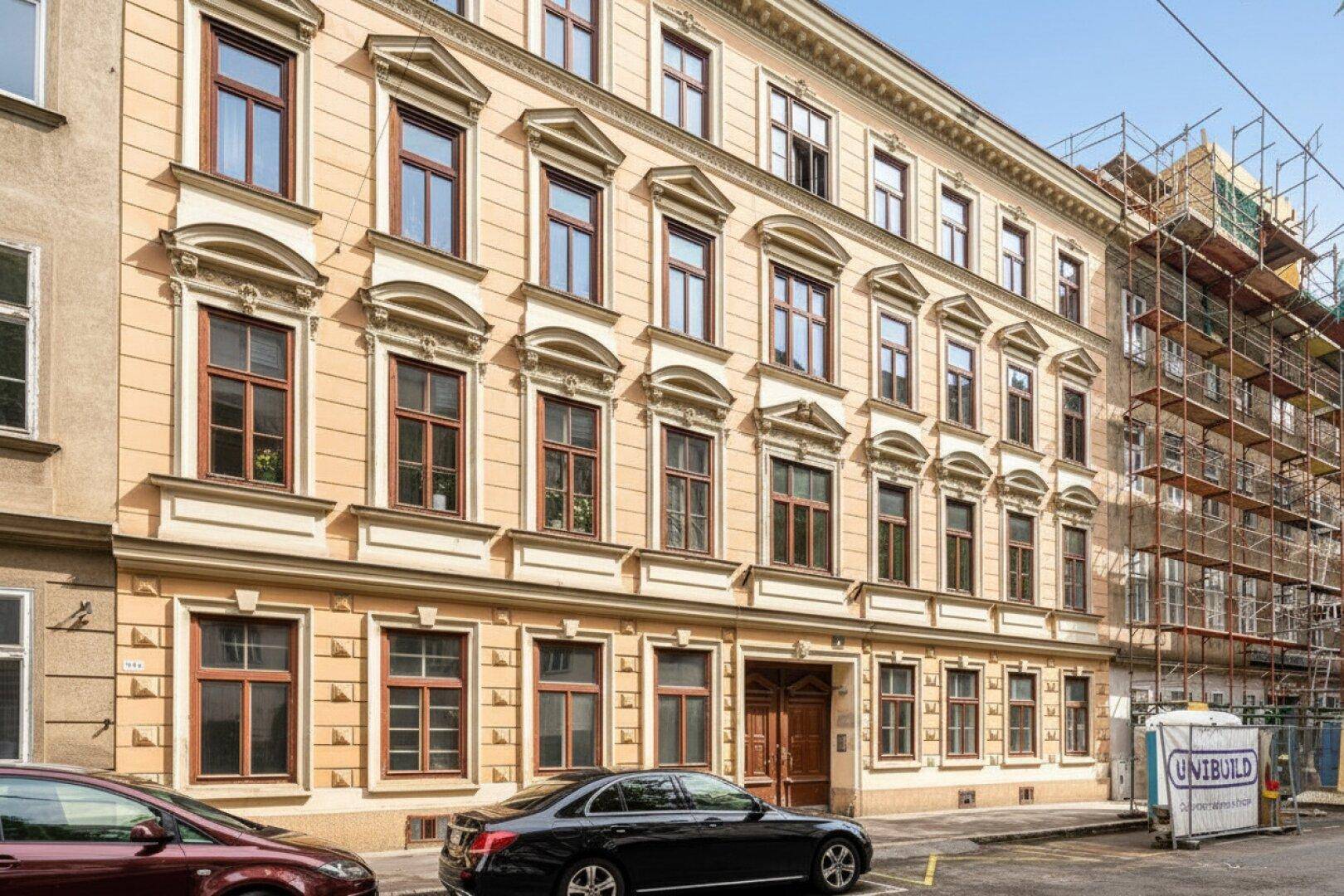 Repräsentative Altbaufassade mit verzierten Fenstern und parkenden Autos, teilweise eingerüstet.