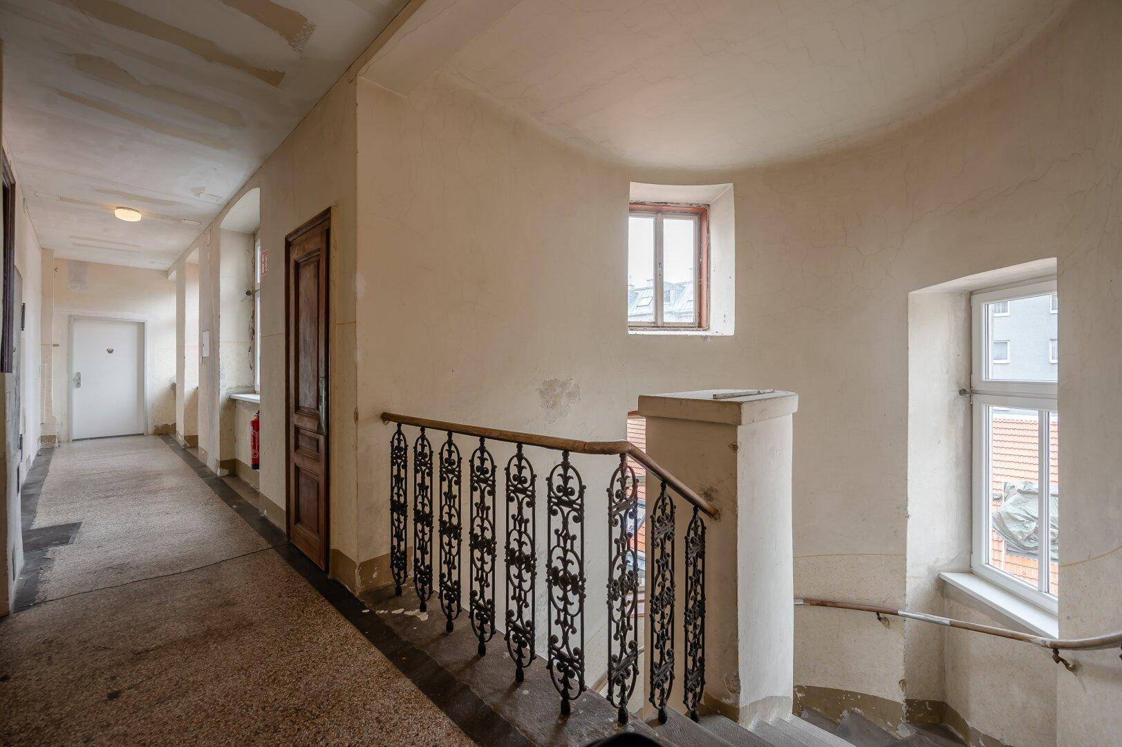Historisches Treppenhaus mit schmiedeeisernem Geländer und langen Fluren, typisch für Altbauten.