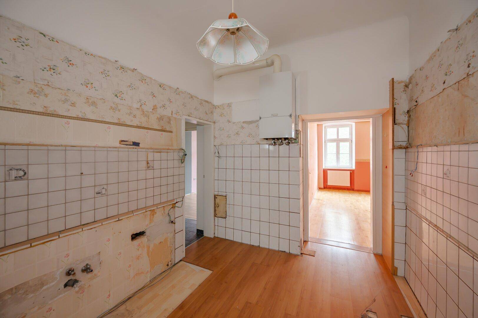 Renovierungsbedürftige Küche mit alten Fliesen und Tapeten, bietet Potenzial für eine moderne Gestaltung.