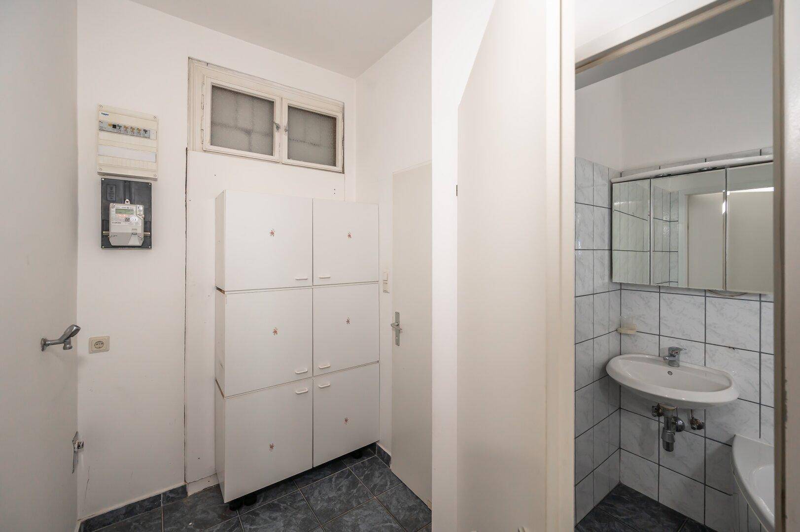 Praktischer Abstellraum mit weißen Schränken und Fenster, angrenzend an ein Badezimmer.