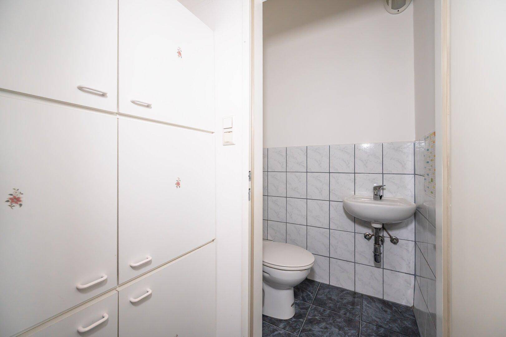 Separates WC mit Toilette und Waschbecken, angrenzend an praktische weiße Schränke.