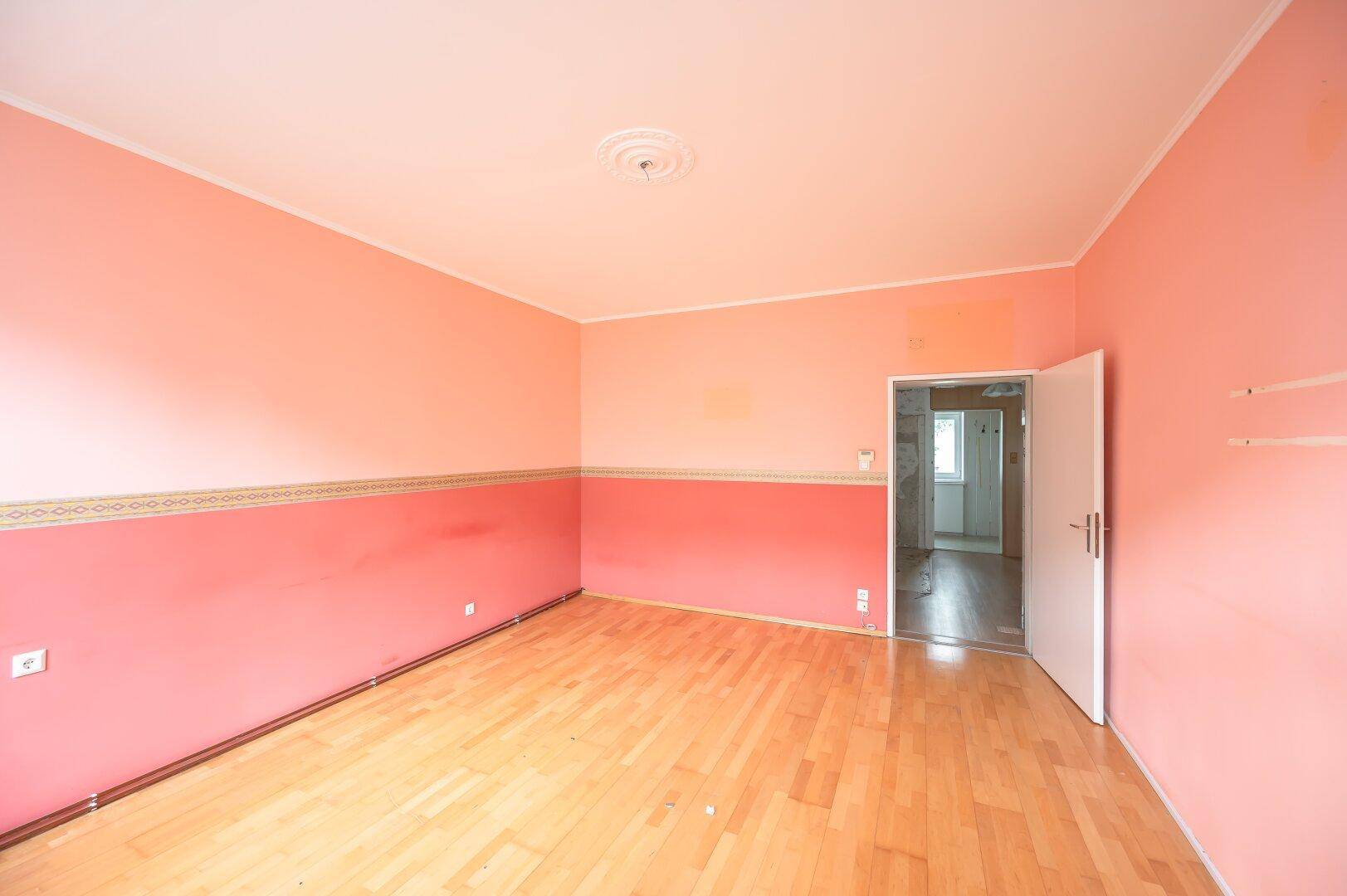 Geräumiges Zimmer mit Holzboden und pfirsichfarbenen Wänden, bietet Zugang zu einem weiteren Raum.