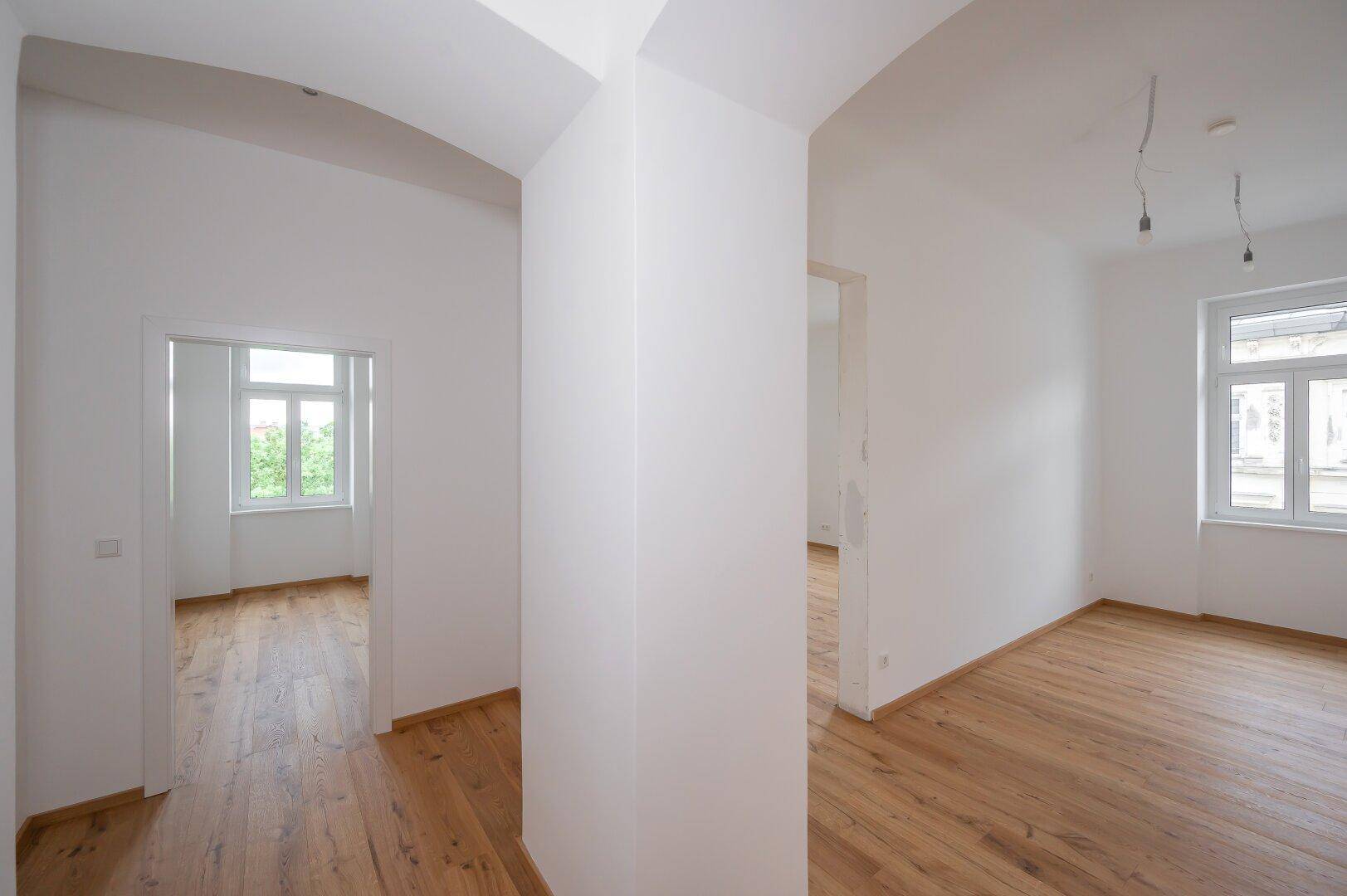 Heller Flur mit Holzboden, der zu verschiedenen Zimmern mit großen Fenstern führt.