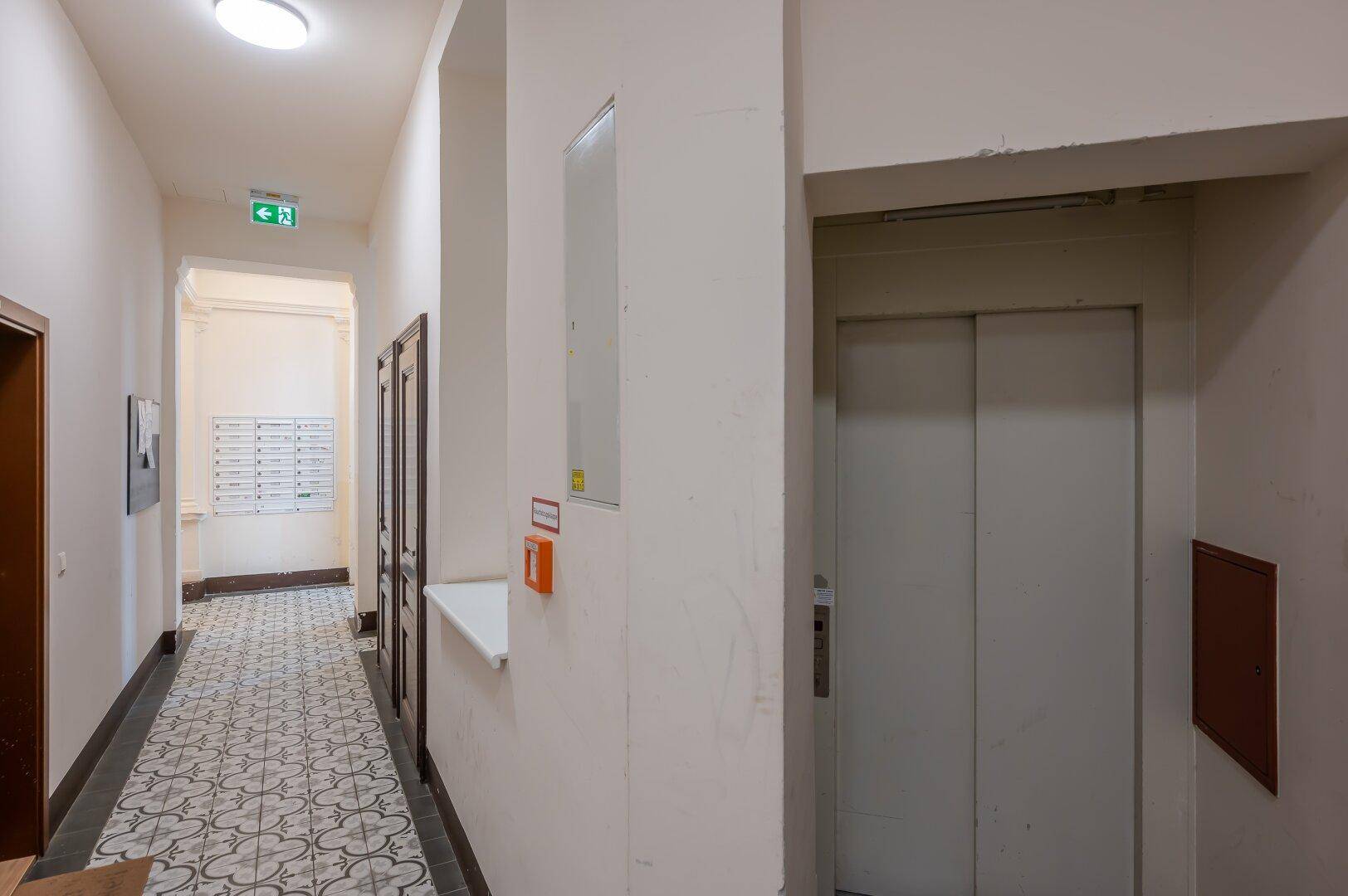 Heller Hausflur mit Aufzug und traditionellen Fliesen, führt zu den Wohnungen.