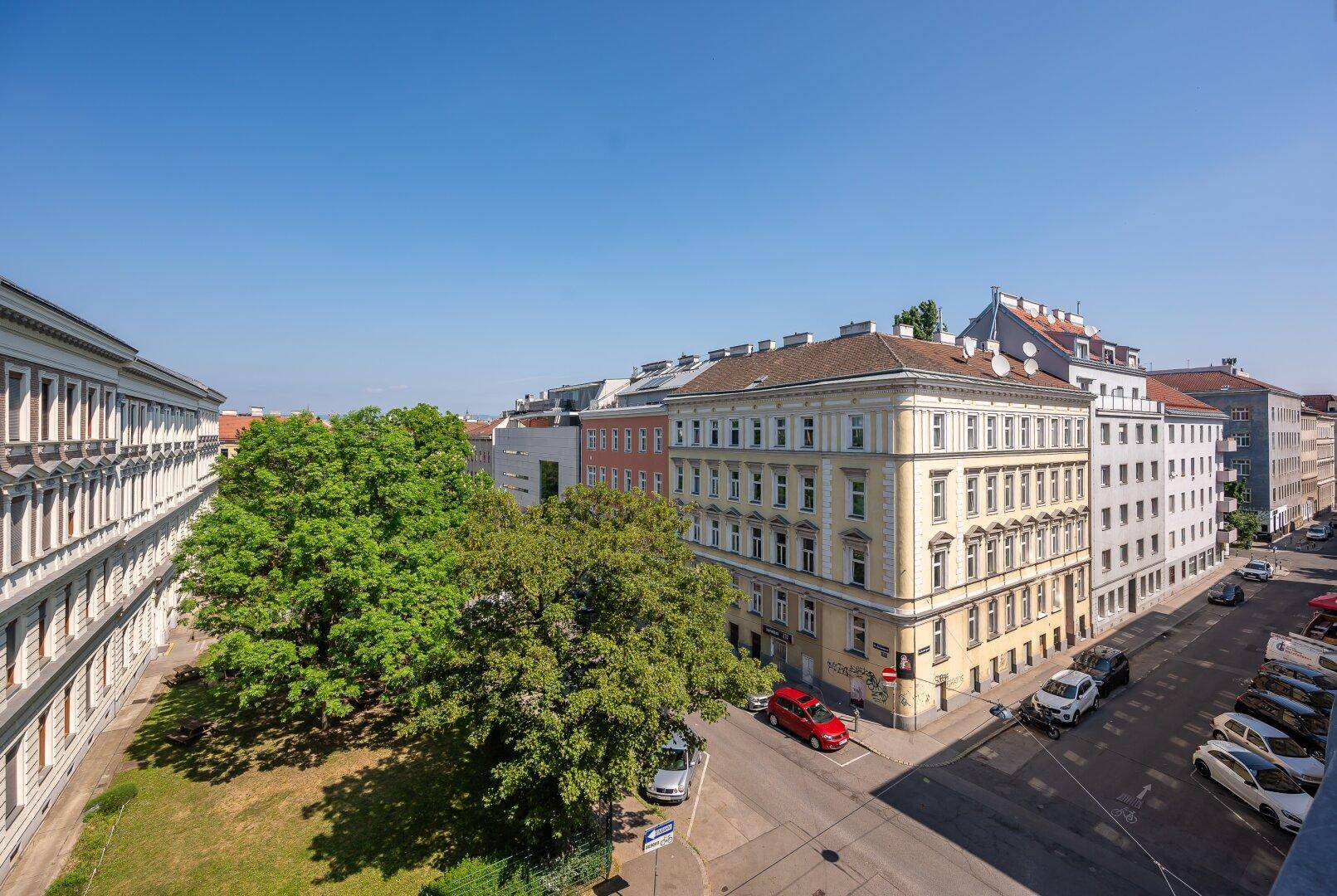 Luftaufnahme einer belebten Stadtstraße mit historischen Gebäuden und viel Grün.
