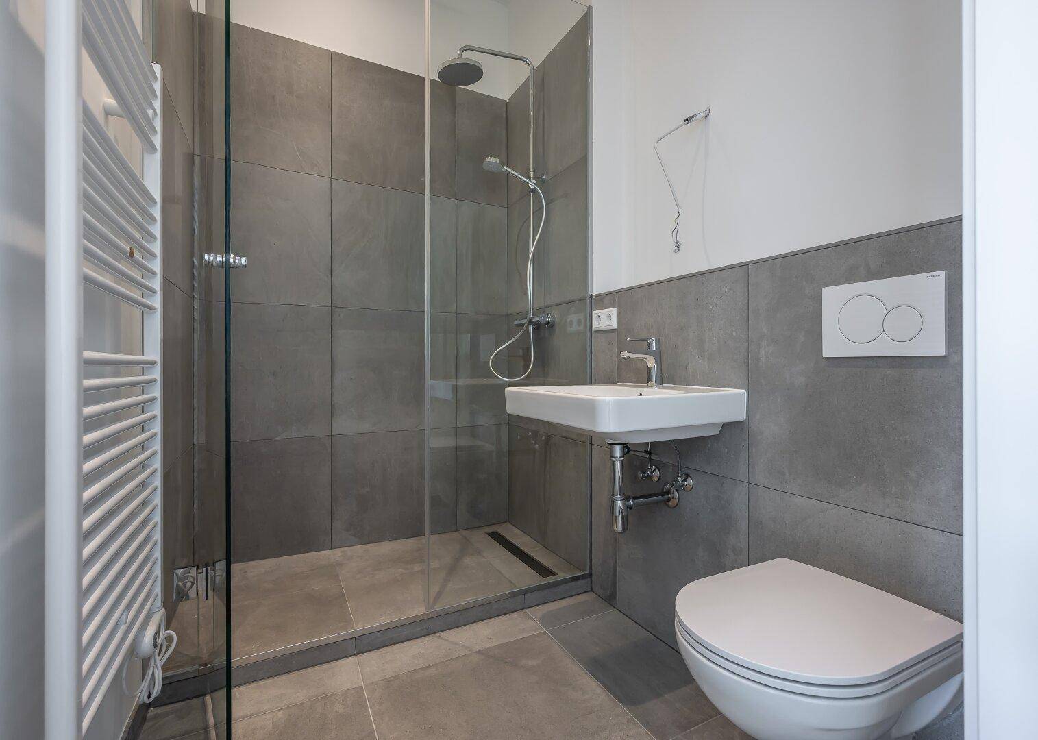 Modernes Badezimmer mit ebenerdiger Dusche, Wand-WC, Waschbecken und beheiztem Handtuchhalter.