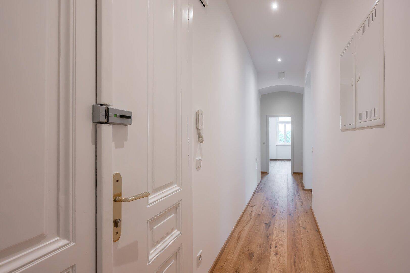 Langer, heller Flur mit Holzboden und Einbaustrahlern, führt zum Eingang der Wohnung.
