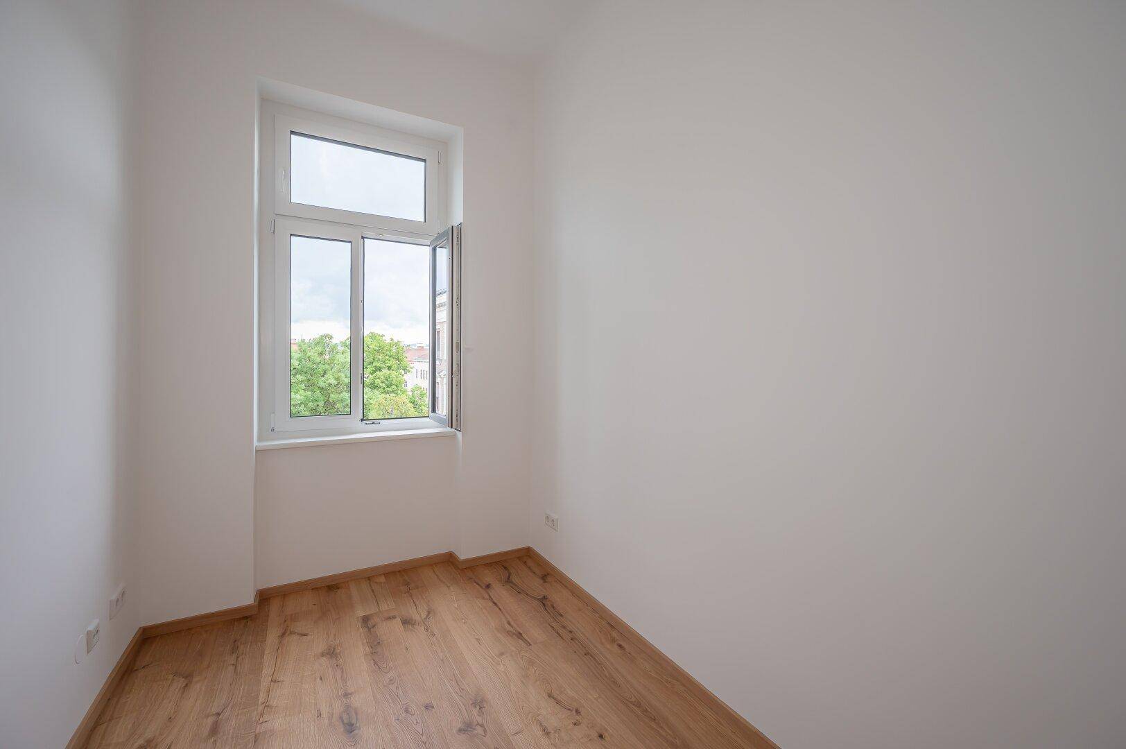 Helles Zimmer mit Holzboden und geöffnetem Fenster, bietet frische Luft und Ausblick.