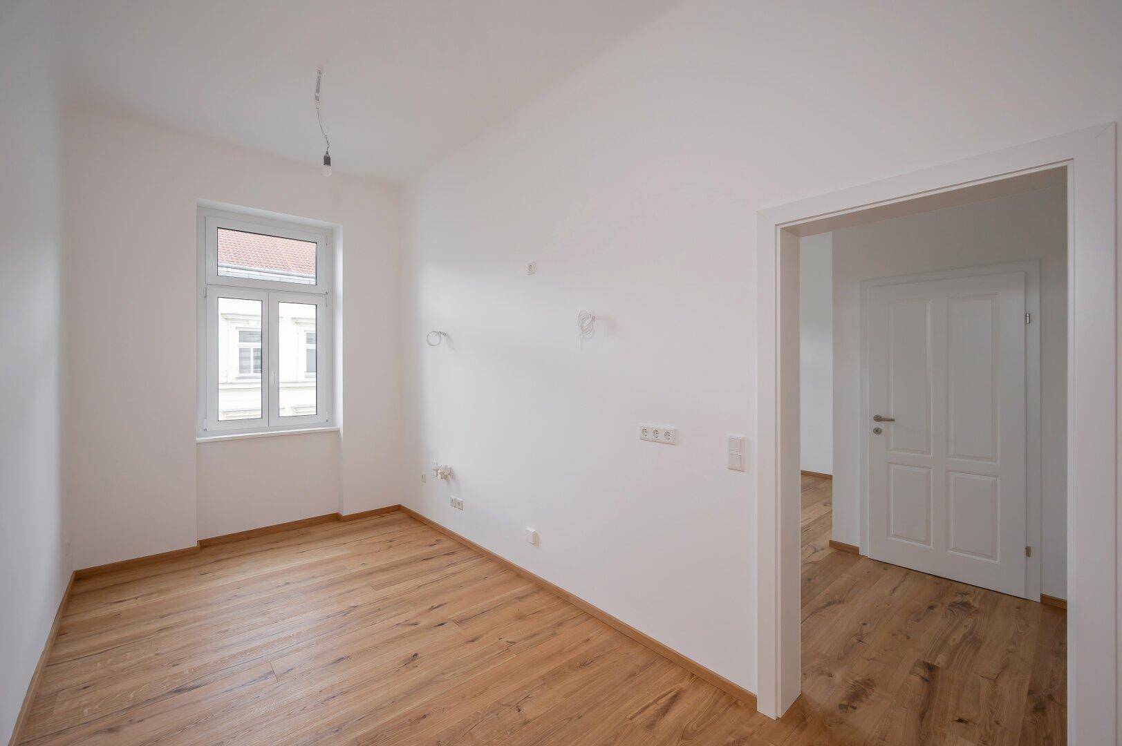 Leeres Zimmer mit Holzboden und einem Fenster, ideal als Schlafzimmer oder Arbeitszimmer.