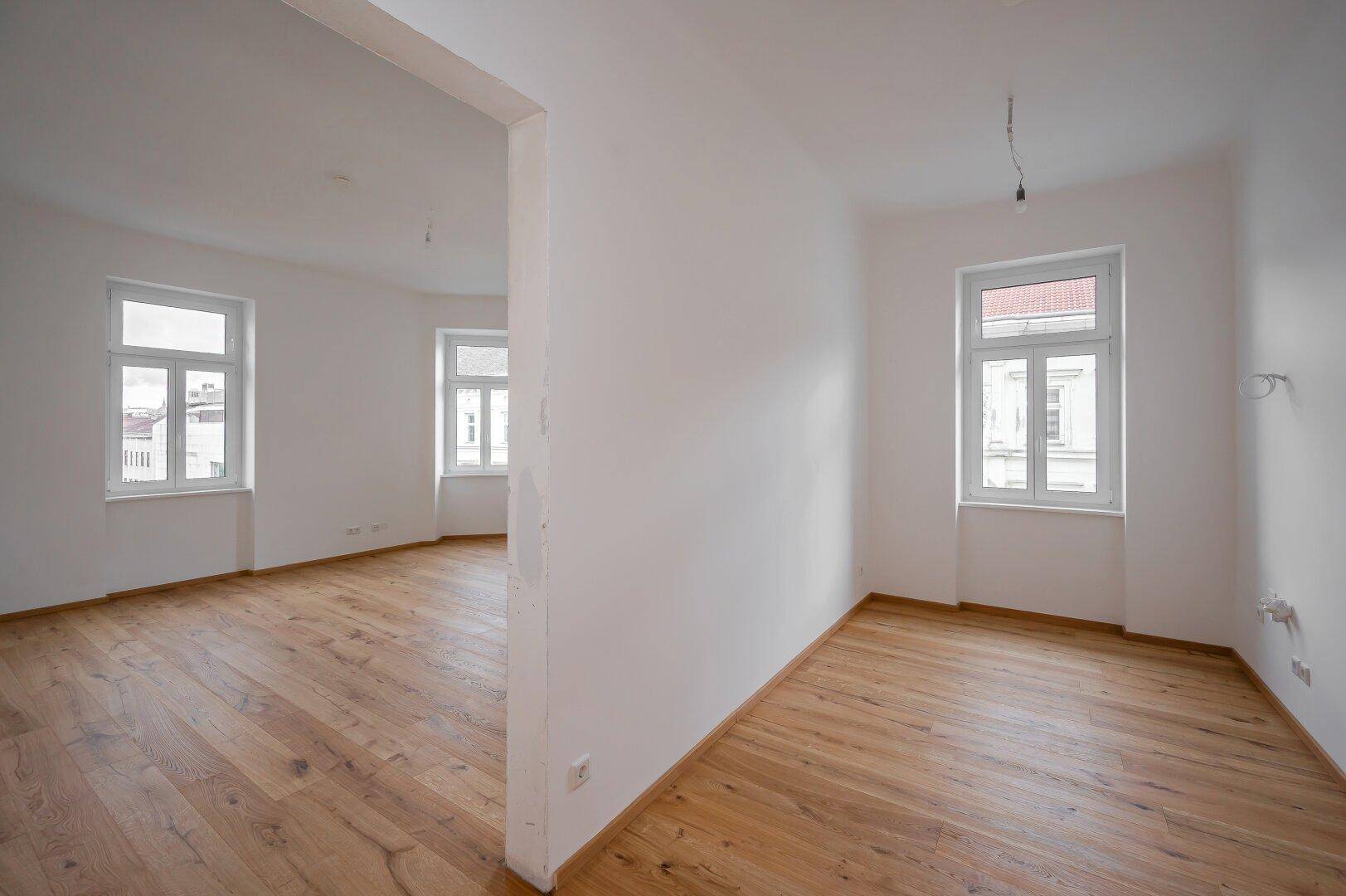 Großer, heller Raum mit Holzboden und mehreren Fenstern, bietet flexible Gestaltungsmöglichkeiten.