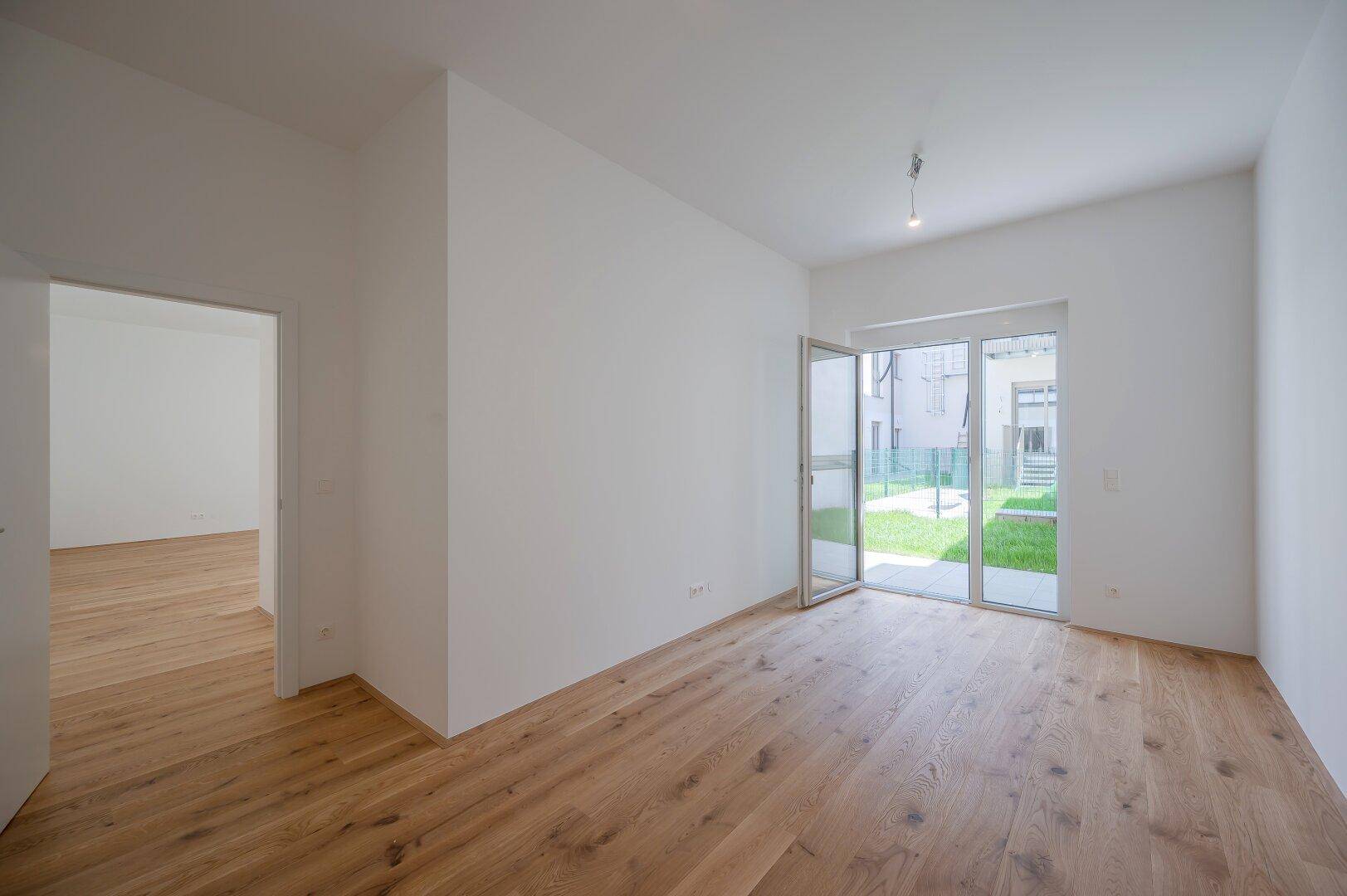 Geräumiges, helles Zimmer mit Holzboden und Blick auf den Garten, ideal für Wohn- oder Schlafbereich.