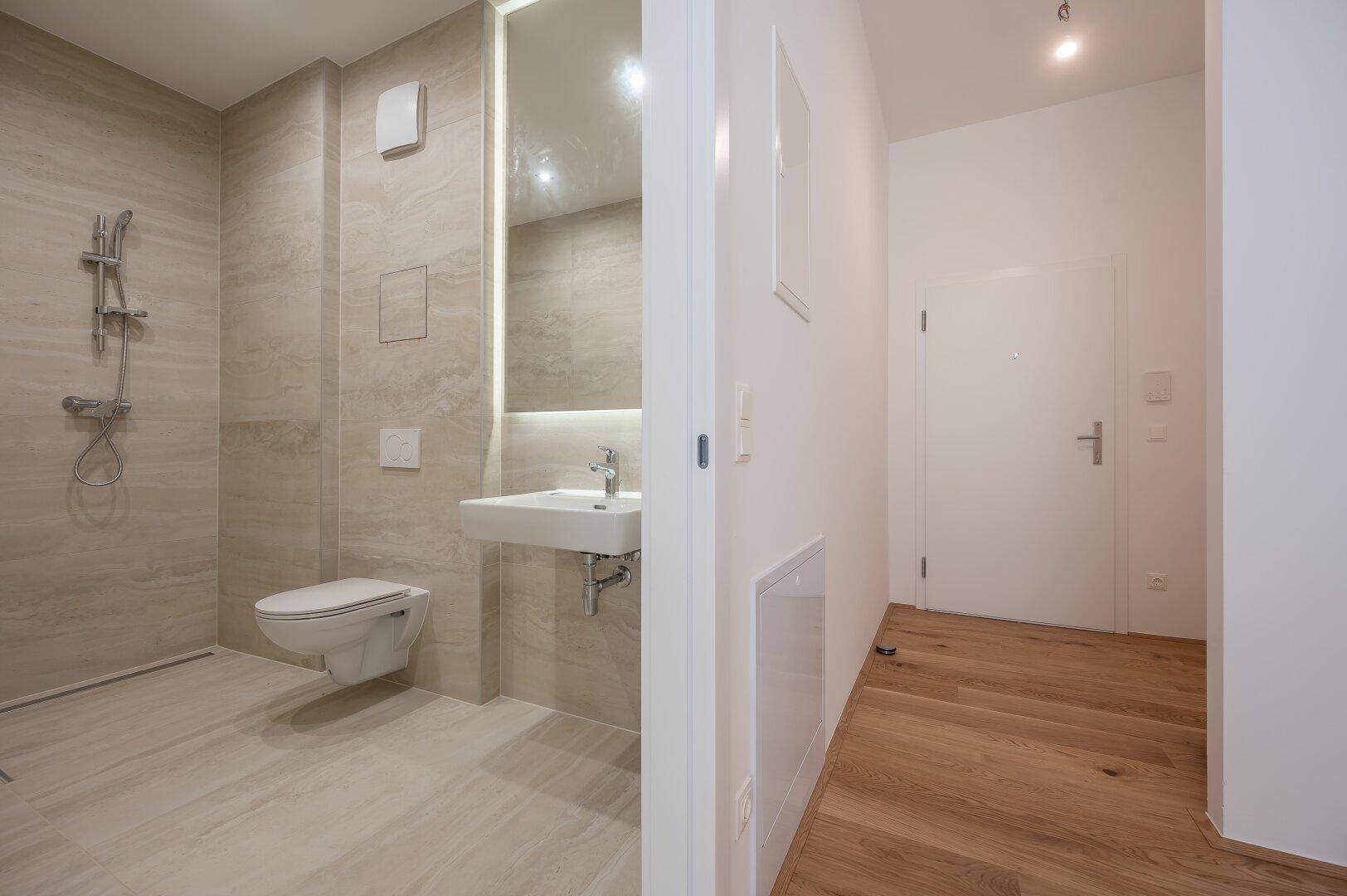Modernes Badezimmer mit beigefarbenen Fliesen und Blick in den angrenzenden Flur.