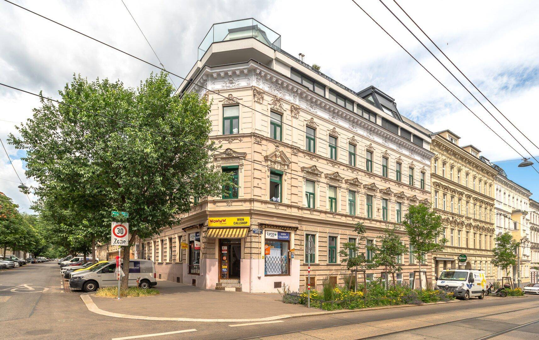 Historisches Eckgebäude mit klassischer Fassade und grünen Fensterläden in städtischer Umgebung.