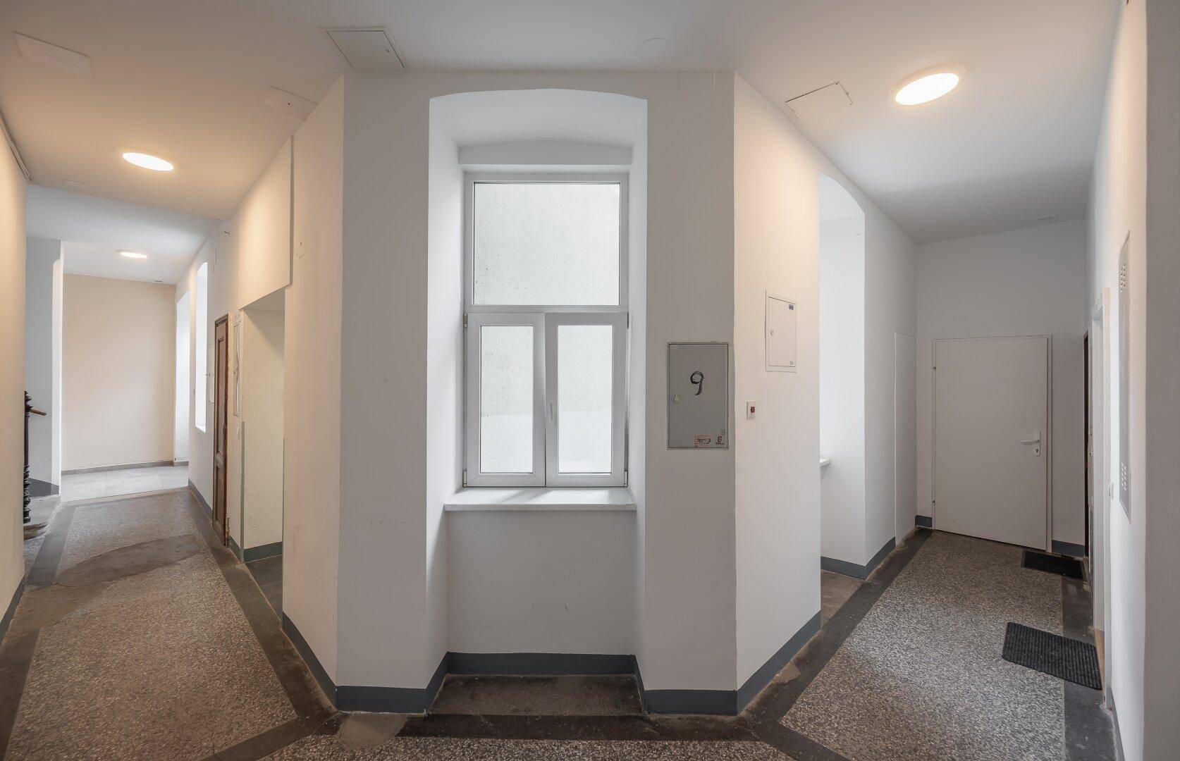 Heller Flur mit Fenster und Terrazzoboden in einem Mehrfamilienhaus.