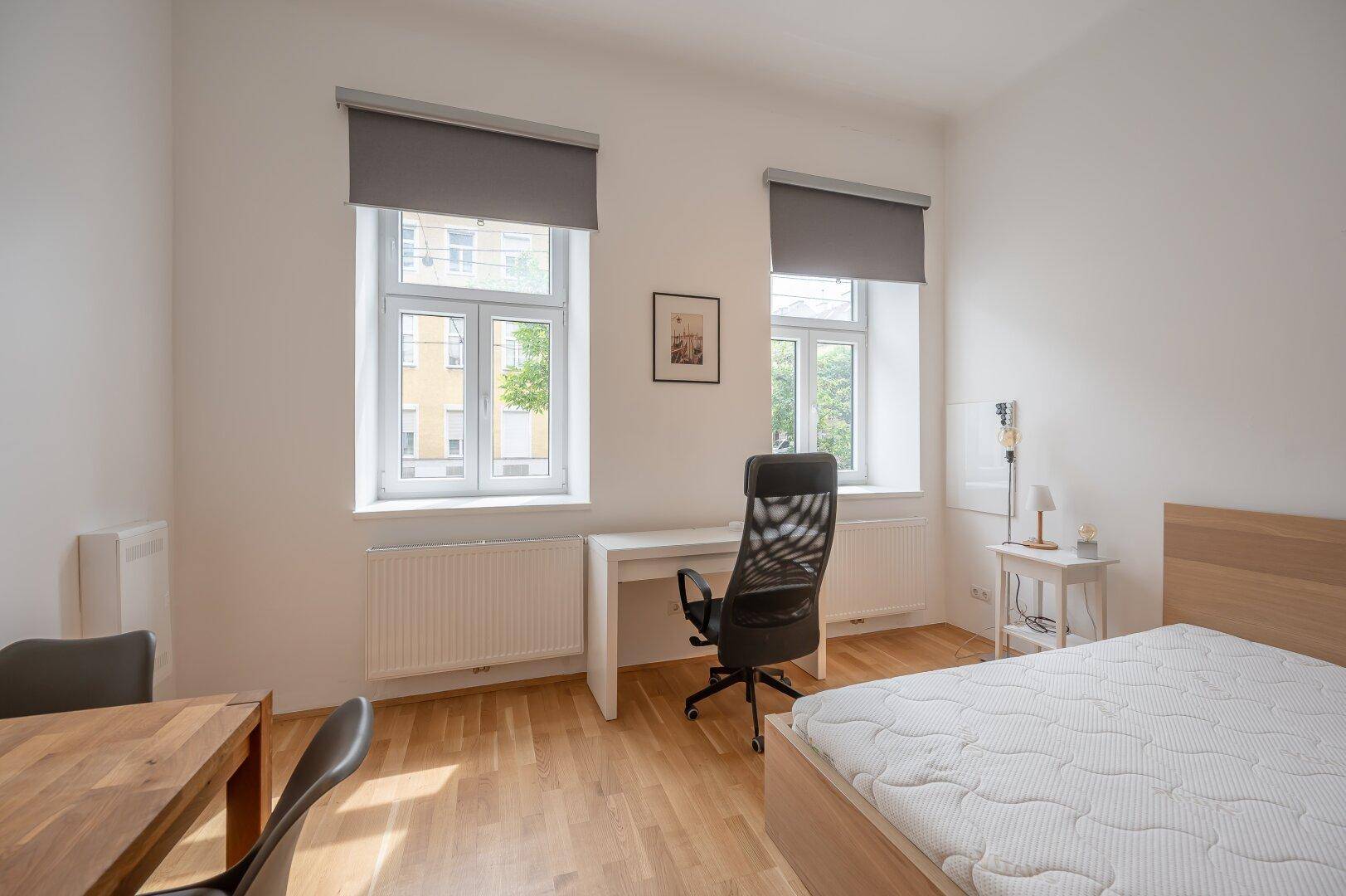 Geräumiges Studiozimmer mit Bett, Schreibtisch und zwei großen Fenstern für viel Tageslicht.