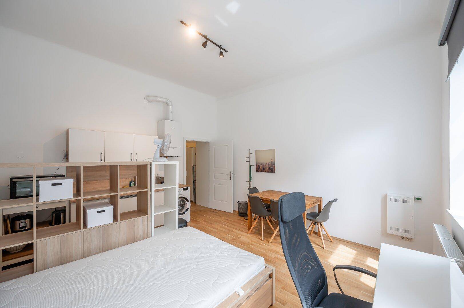 Studio-Apartment mit Schlafbereich, Bücherregal und Essplatz, alles in einem hellen Raum.