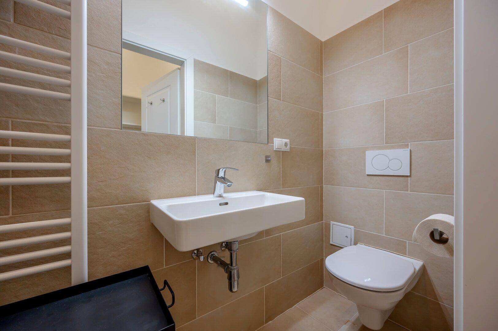 Zeitgemäßes Badezimmer mit wandhängendem WC, Waschbecken und großem Spiegel.