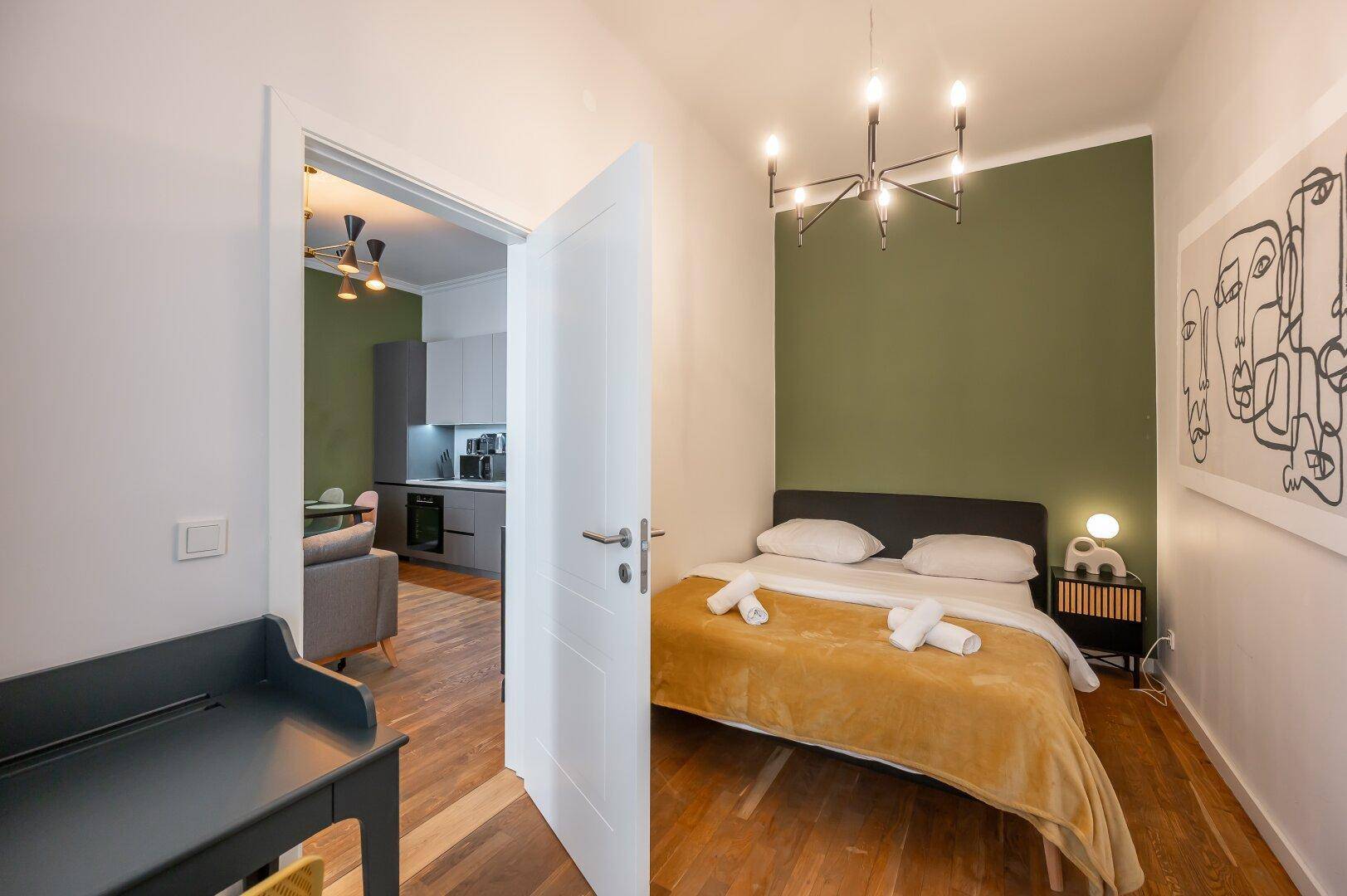 Gemütliches Schlafzimmer mit grüner Akzentwand und Holzboden, verbunden mit dem Wohnbereich.