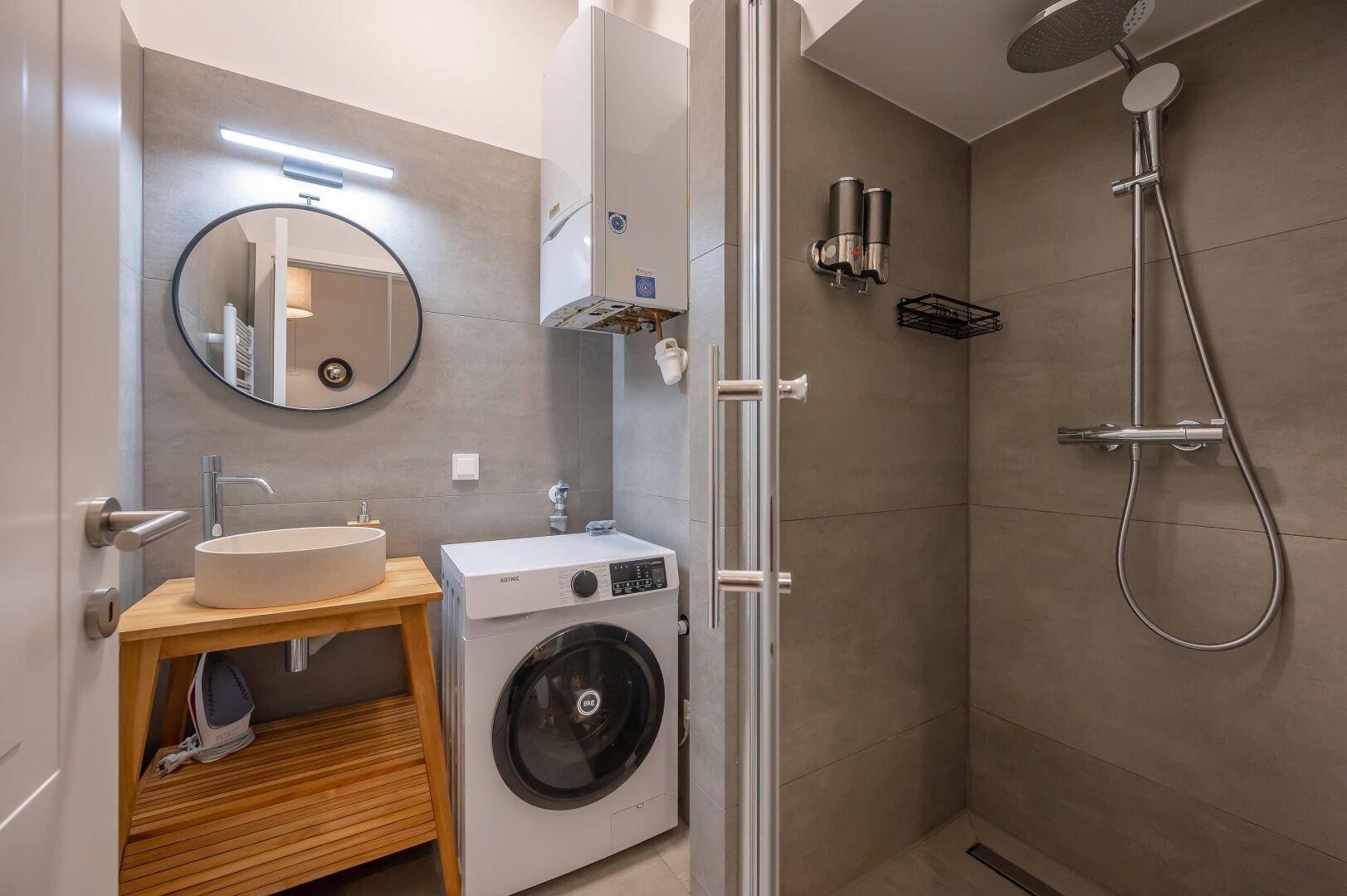 Modernes Badezimmer mit ebenerdiger Dusche, Waschmaschine und stilvollem Waschbecken.