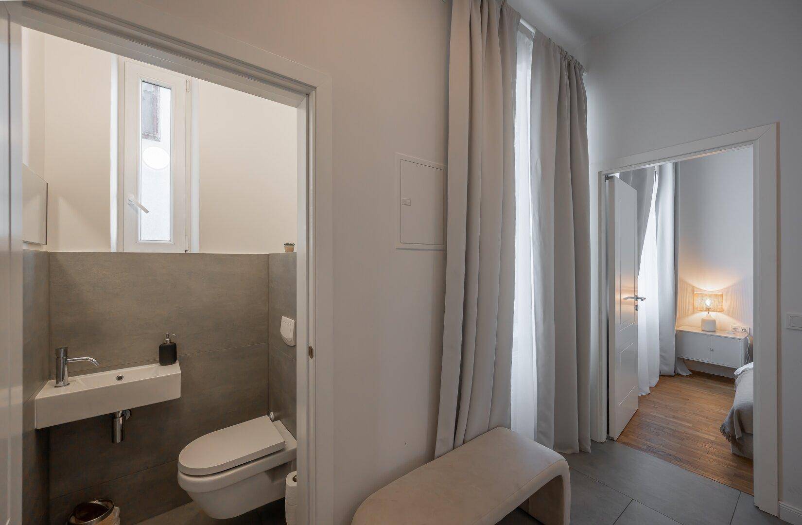 Separates Gäste-WC mit modernem Wand-WC, kleinem Waschbecken und Fenster.