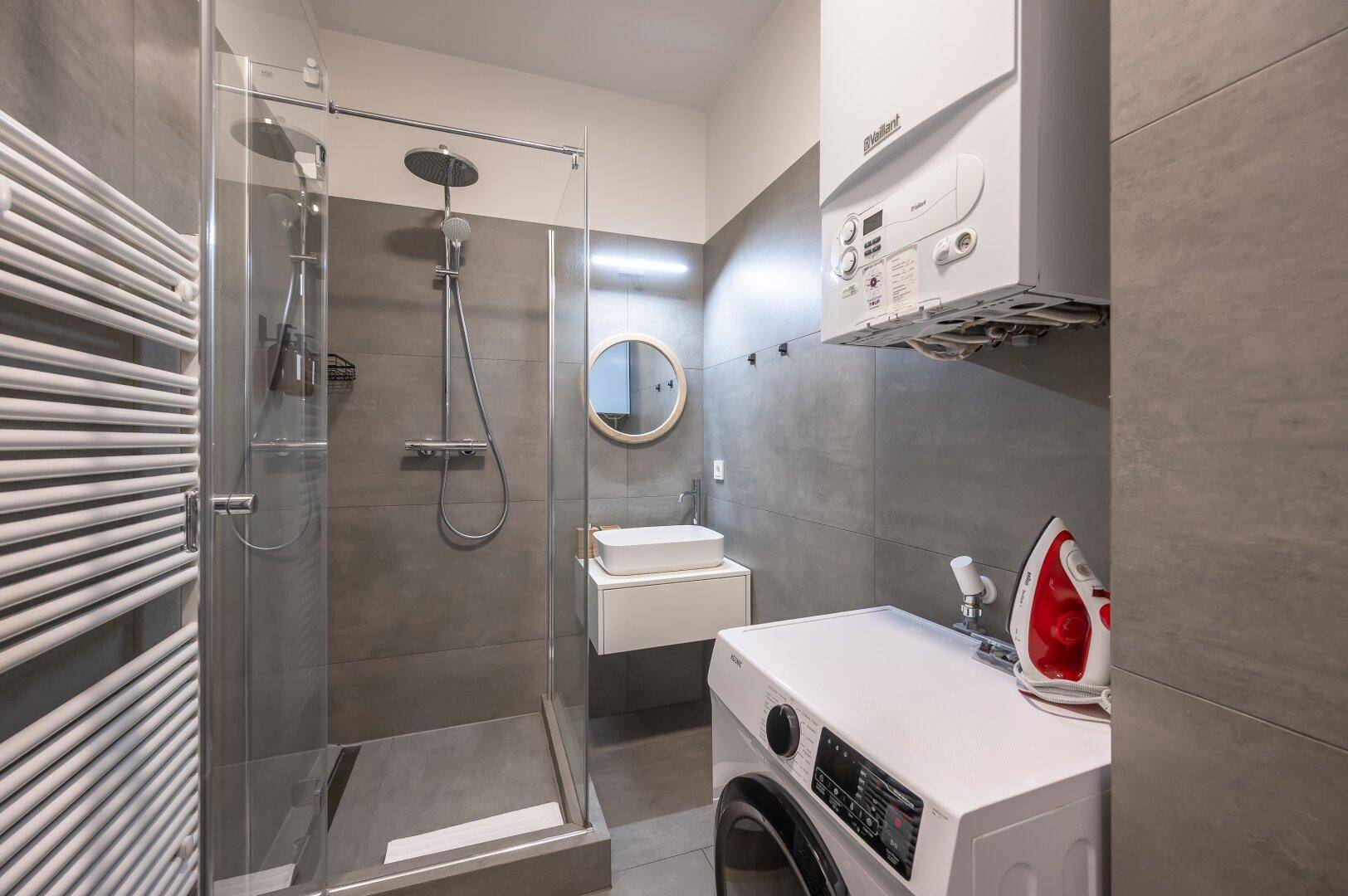 Funktionales Badezimmer mit Duschkabine, Waschmaschine, Heizkörper und Gastherme.