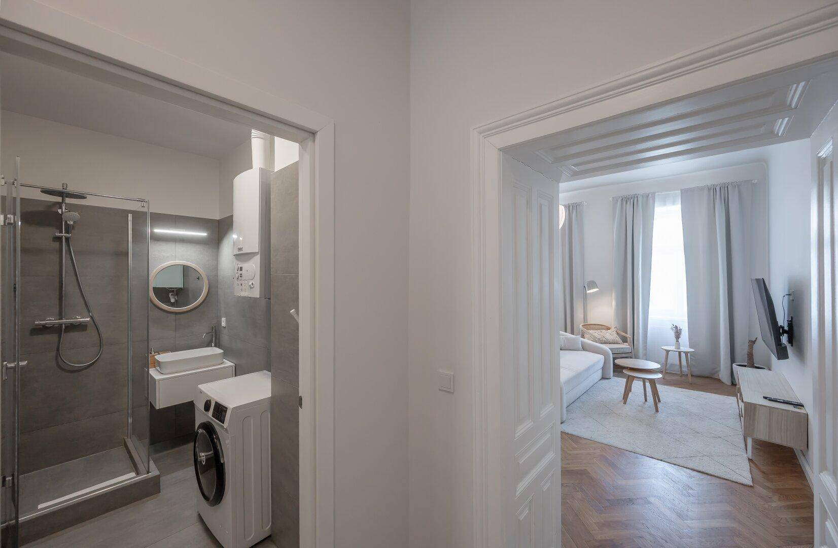Modernes Badezimmer mit Duschkabine, Waschmaschine und Blick in den Wohnbereich.