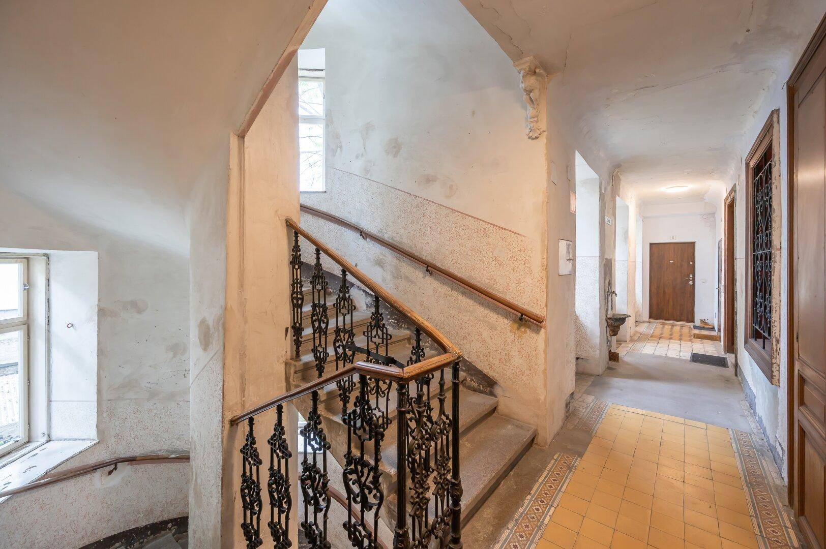 Historisches Treppenhaus mit schmiedeeisernem Geländer, Holzhandlauf und dekorativen Fliesen im Eingangsbereich.