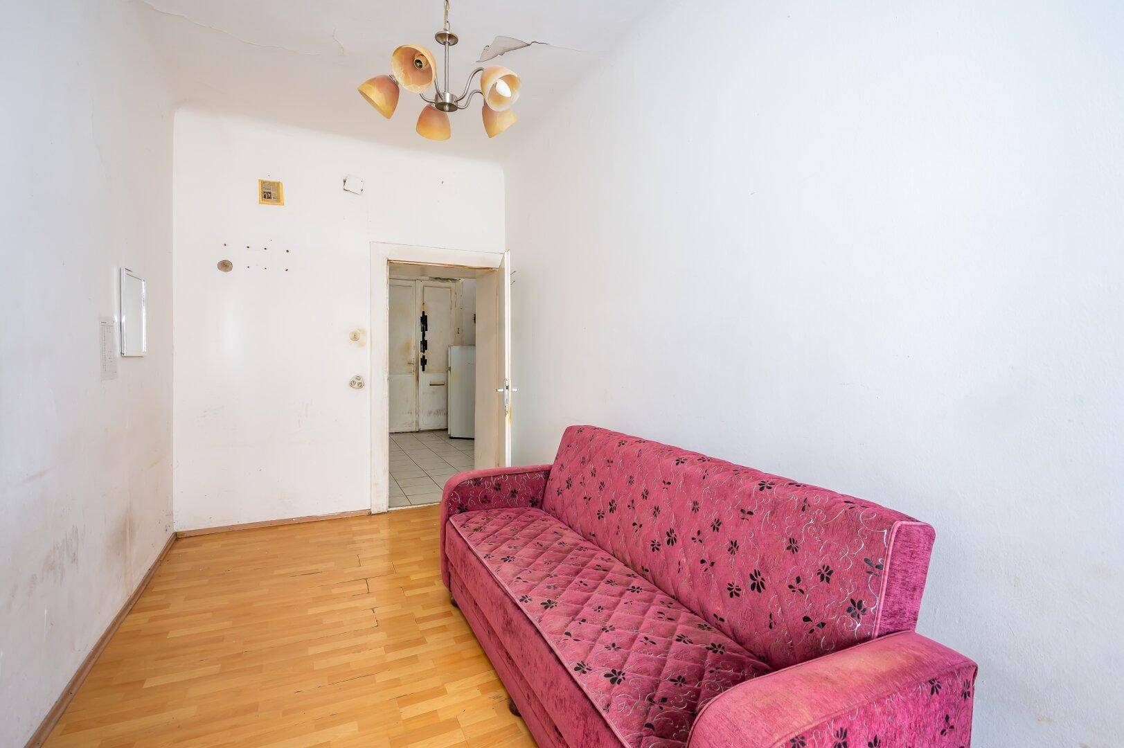 Wohnzimmer mit rotem Sofa und Holzboden, das zu einem weiteren Raum mit Fliesenboden führt.