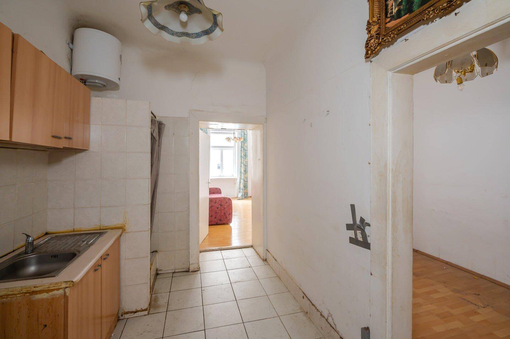 Blick aus der einfachen Küche mit Fliesenboden in das angrenzende Zimmer mit Holzfußboden.