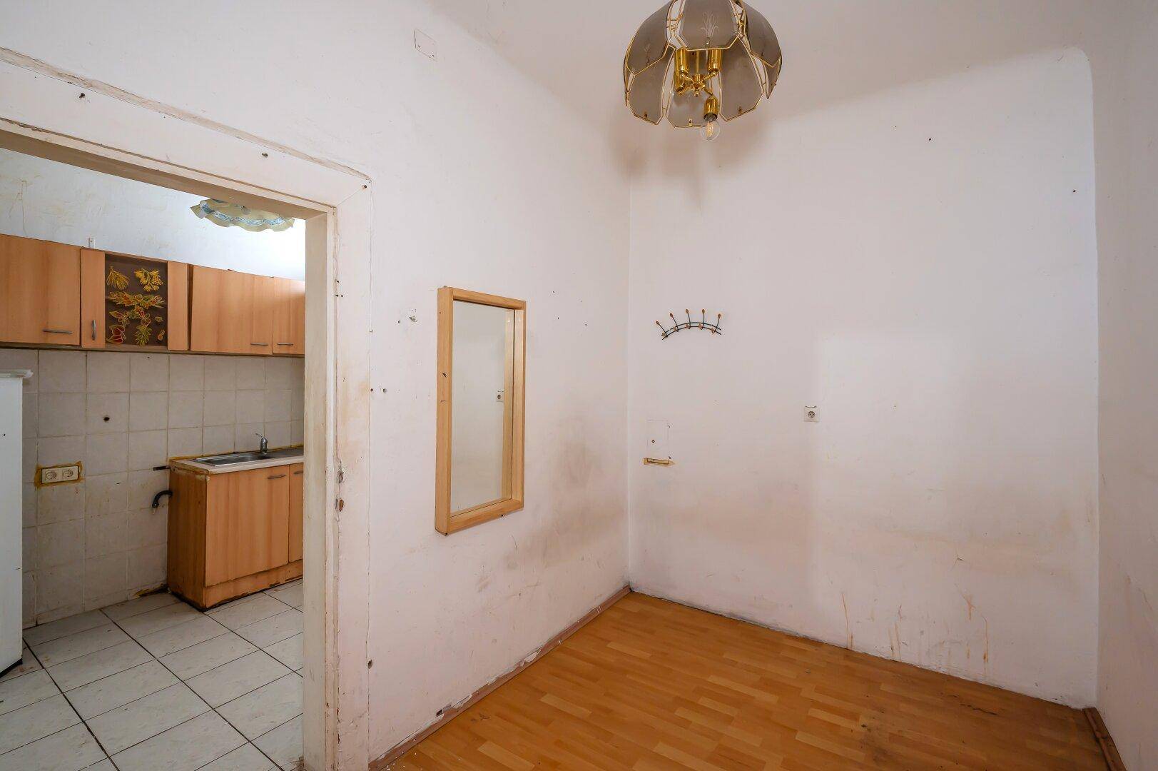Zimmer mit Holzboden und einem Spiegel an der Wand, das zur kleinen Küche führt.