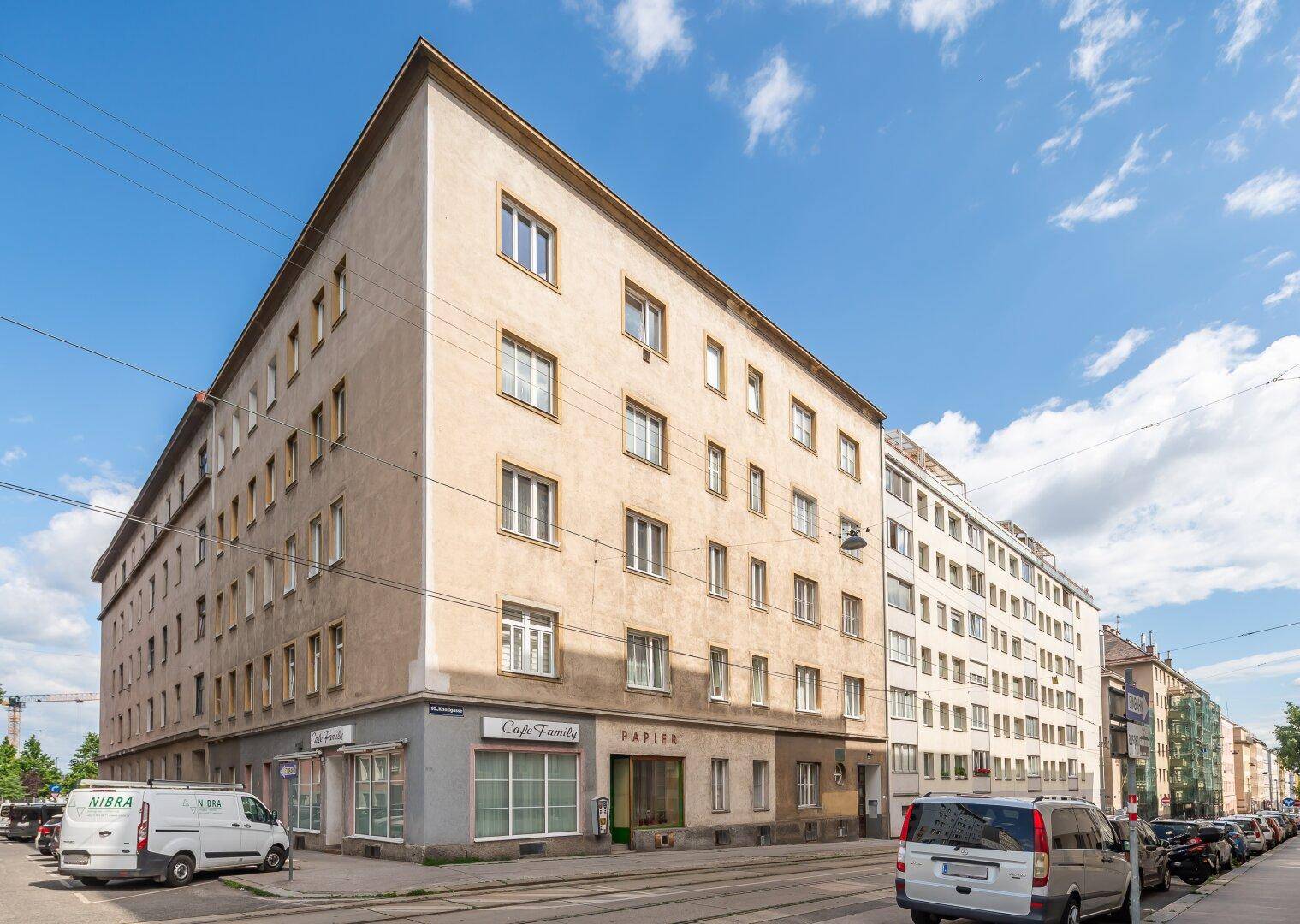 Eckgebäude mit Geschäften im Erdgeschoss und Wohnungen darüber, an einer belebten Straße gelegen.