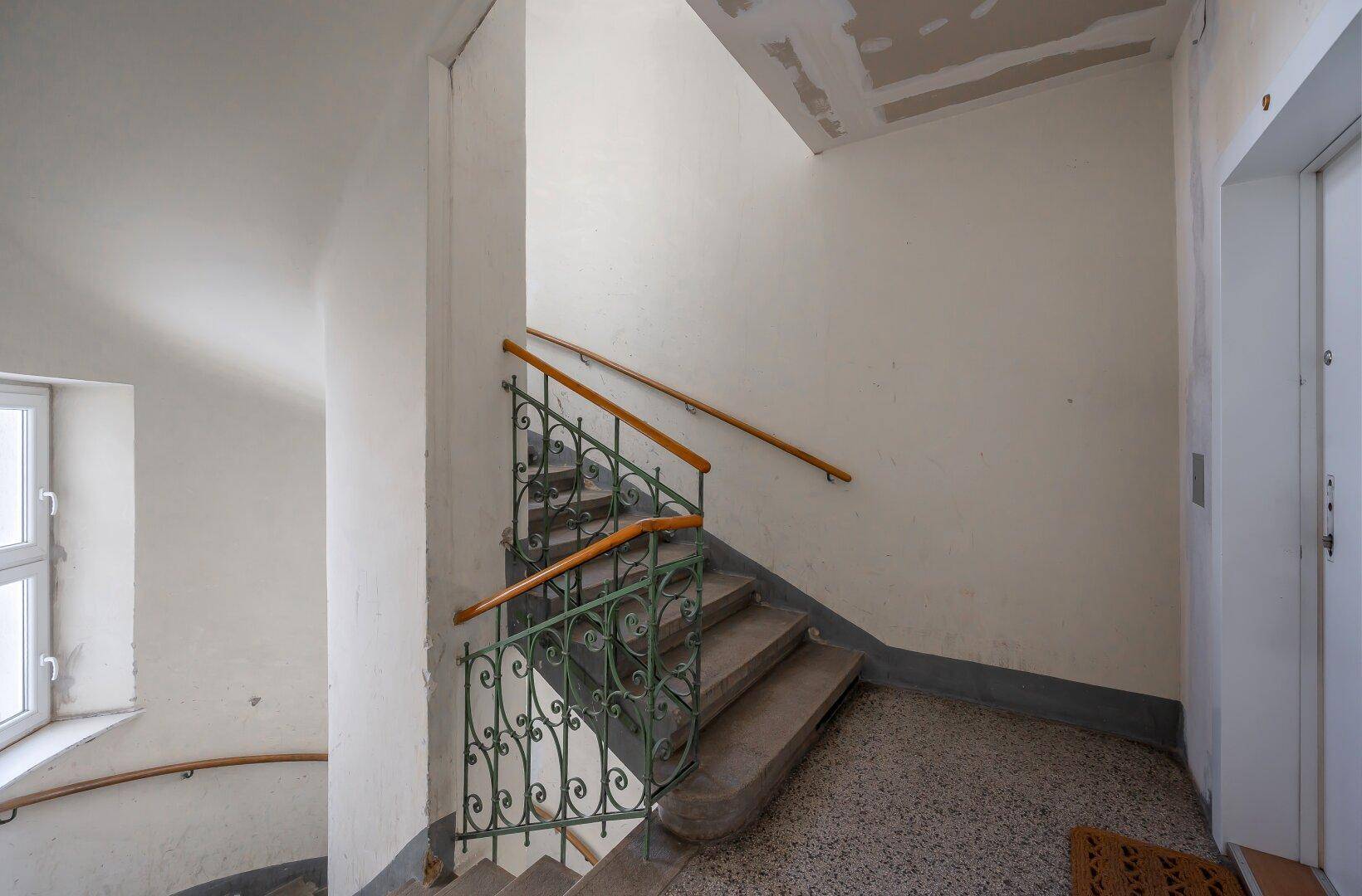 Historisches Treppenhaus mit schmiedeeisernem Geländer und Terrazzoboden in einem Altbau.