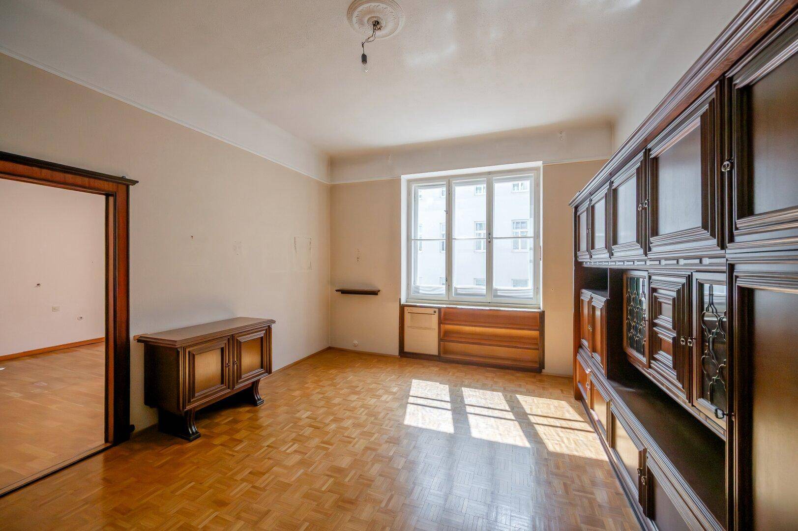 Wohnraum mit klassischem Parkettboden und großem Holzschrank, bietet viel Stauraum und Potenzial.
